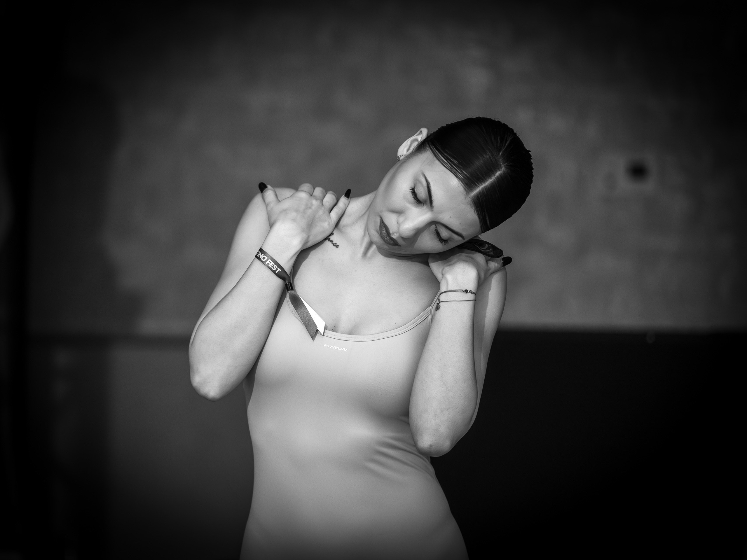 Black and white portrait of a woman with eyes closed holding her neck indoors.