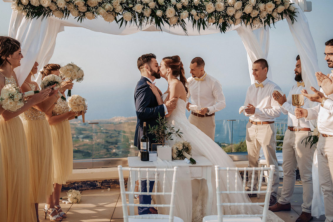 Символическая свадебная церемония в Греции на Крите, пара целуется в свадебной арке. Фотограф Екатерина Романова, свадьба.