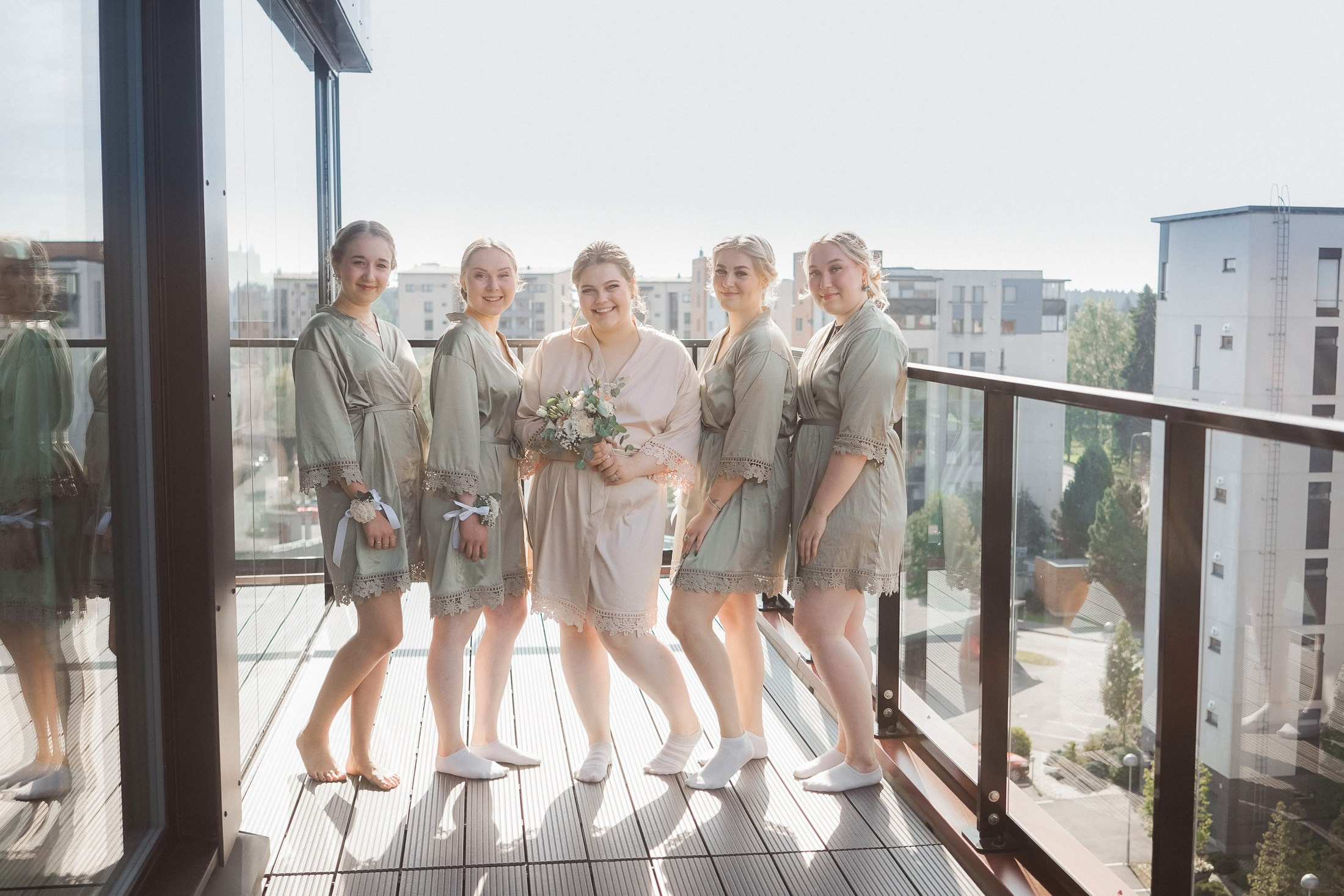 Bride and bridesmaids in robes on a teracce, by a Helsinki wedding photographer