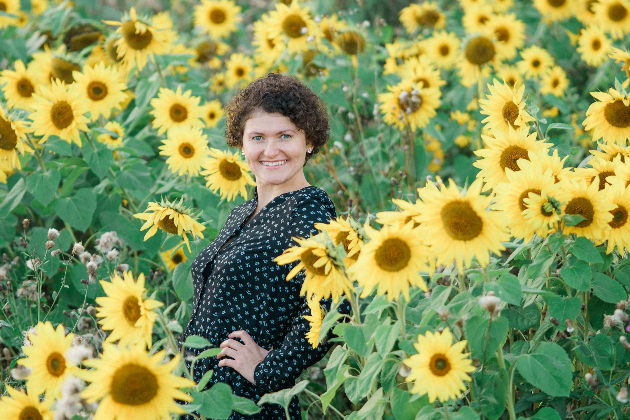 Iloinen ja hymyilevä nainen auringonkukka pellon keskellä.