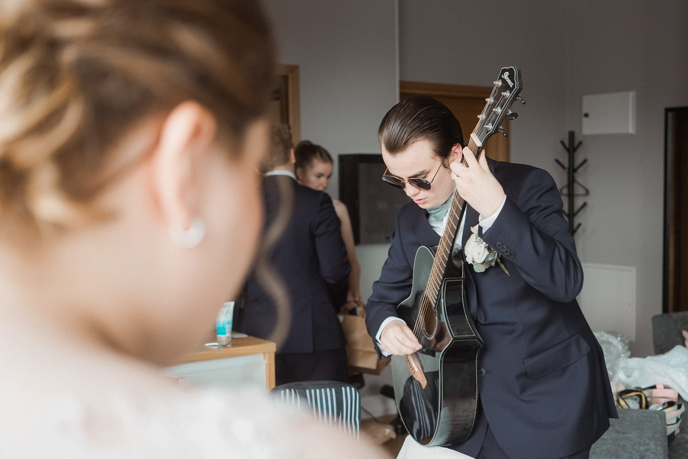 Groom rehearsing a song on guitar during a shared getting-ready morning