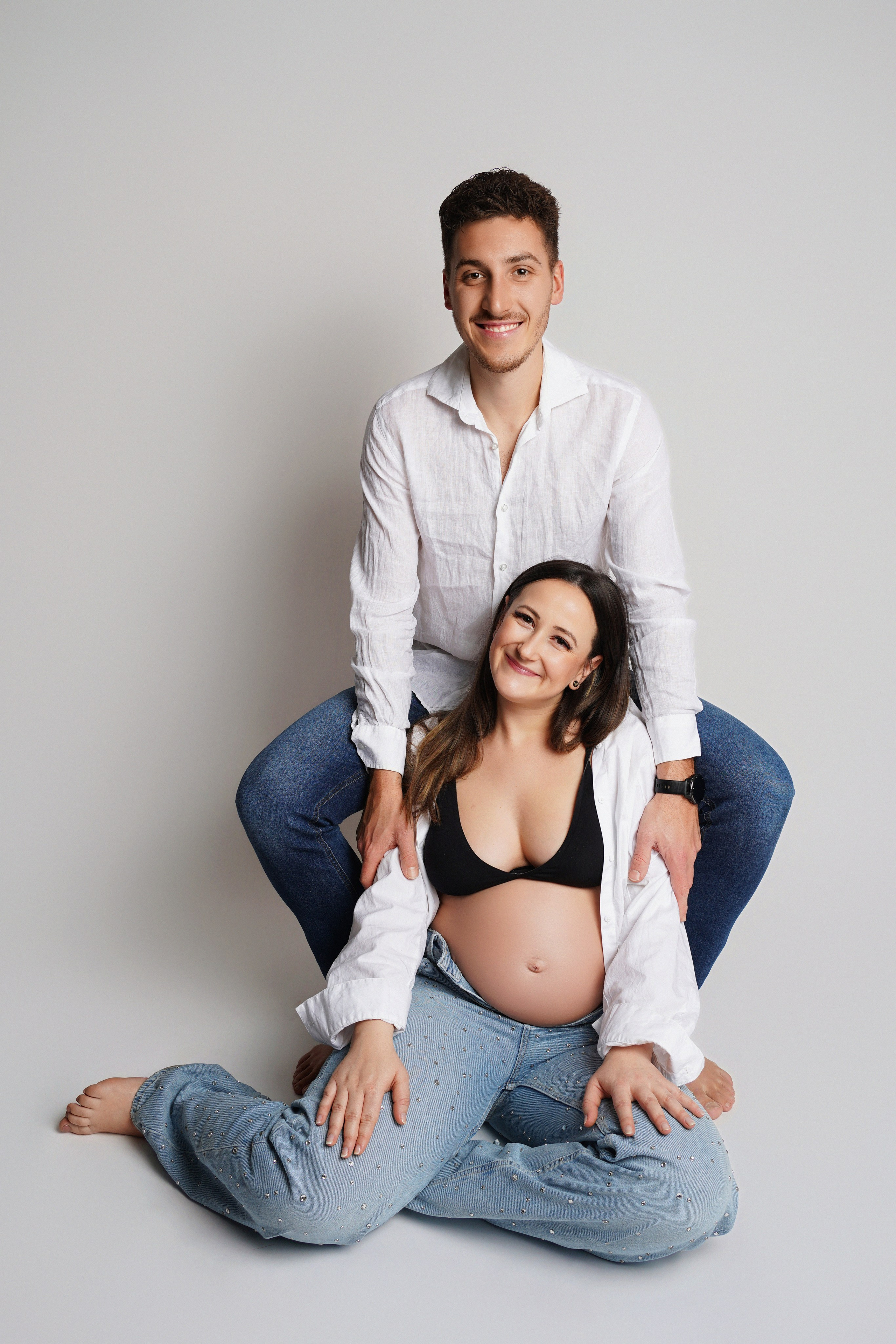 Glückliches Paar m Partnerlook mit Hemden und Jeans im Fotostudio beim Schwangerschaftshoot Augsburg 