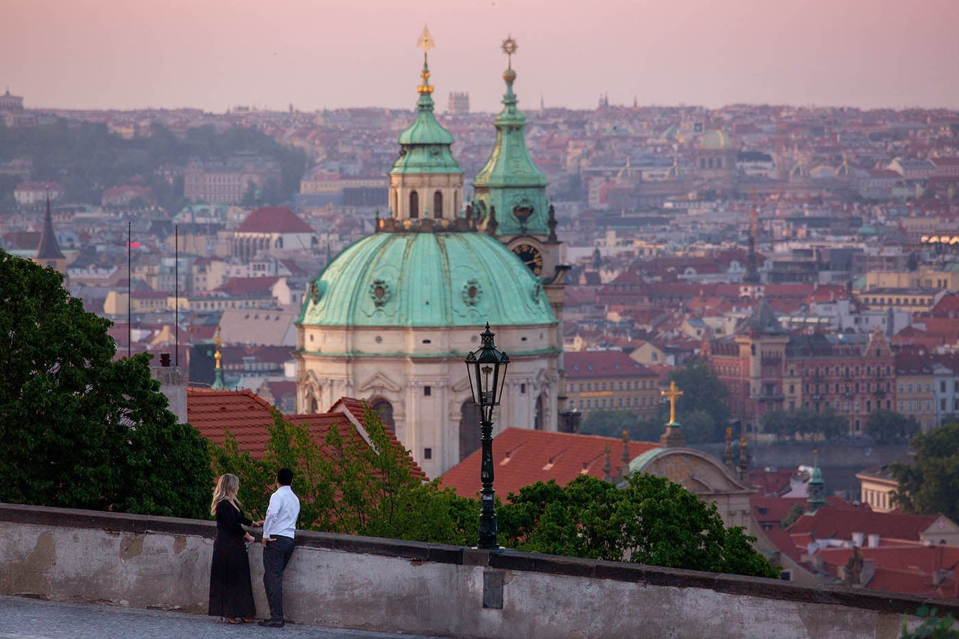 A couple overlooking Malá Strana from Prague Castle at sunrise, with panoramic views of Prague below
