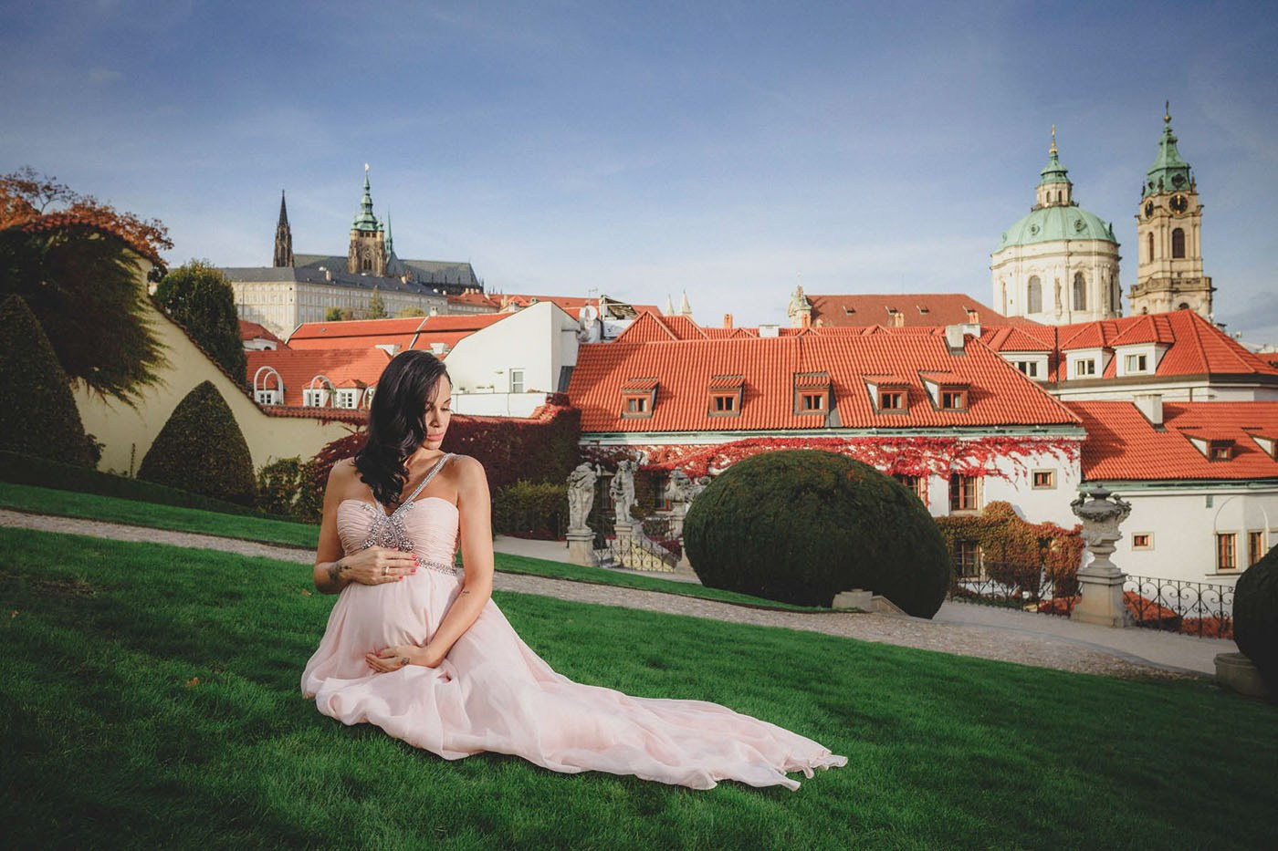 Pregnant woman seated on the lawn at Vrtba Garden with Prague Castle behind