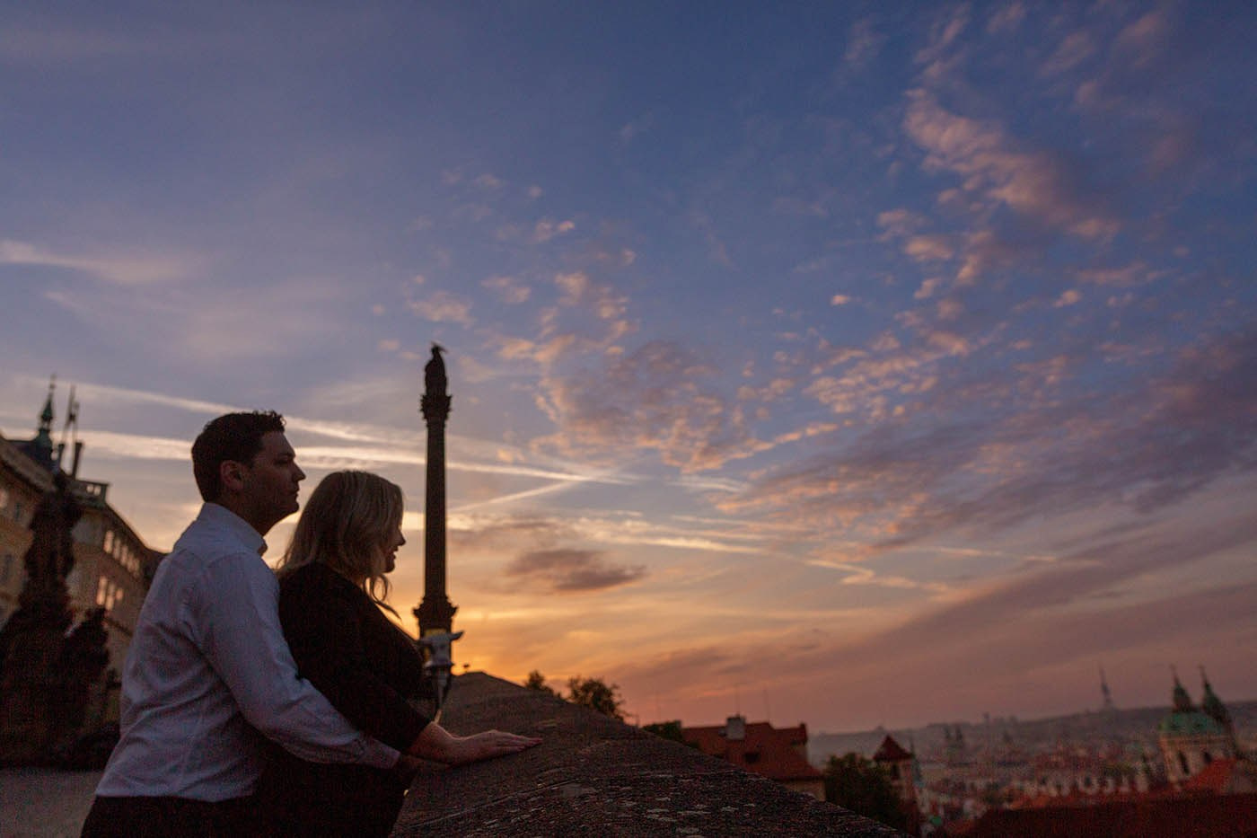 A couple watching the sunrise light illuminate the red rooftops of Malá Strana from Prague Castle