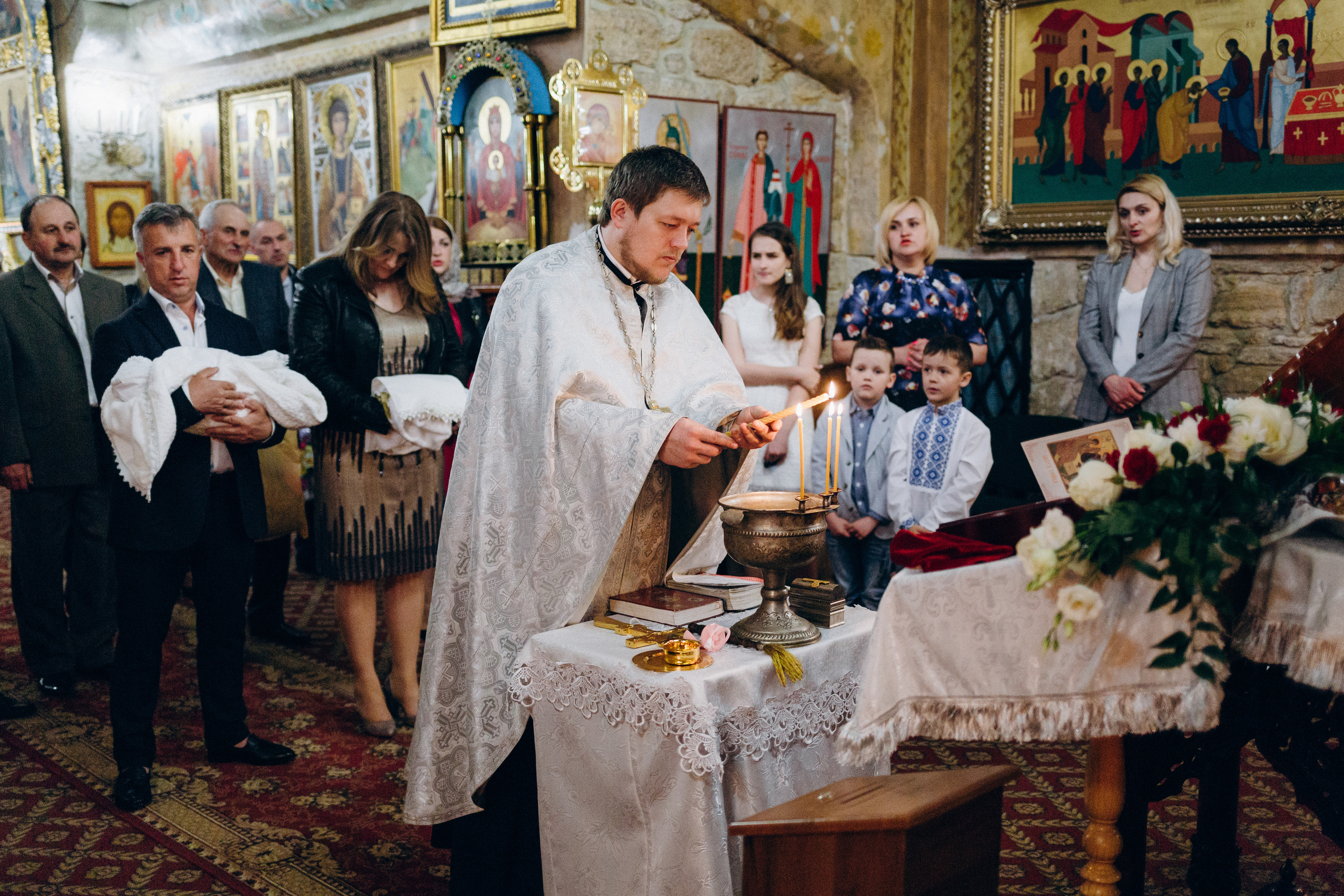 Фотозйомка хрестин. Священник запалює свічки під час таїнства Хрещення 