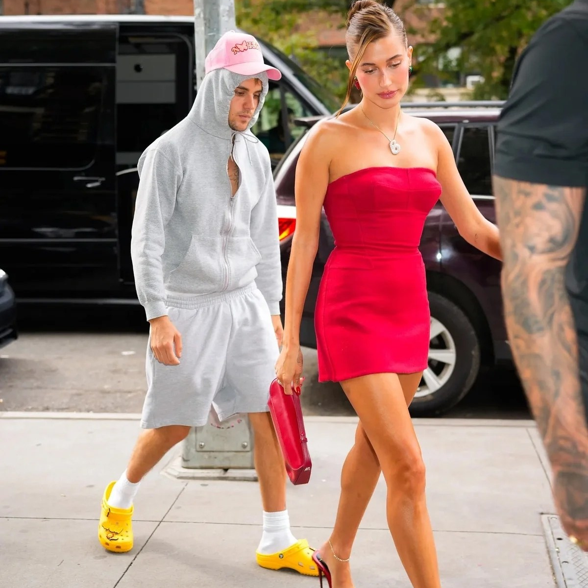 Джастин Бибер в сером худи, шортах и жёлтых Crocs с носками и Хейли Бибер в красном мини-платье и красных босоножках идут по улице Нью-Йорка 2025