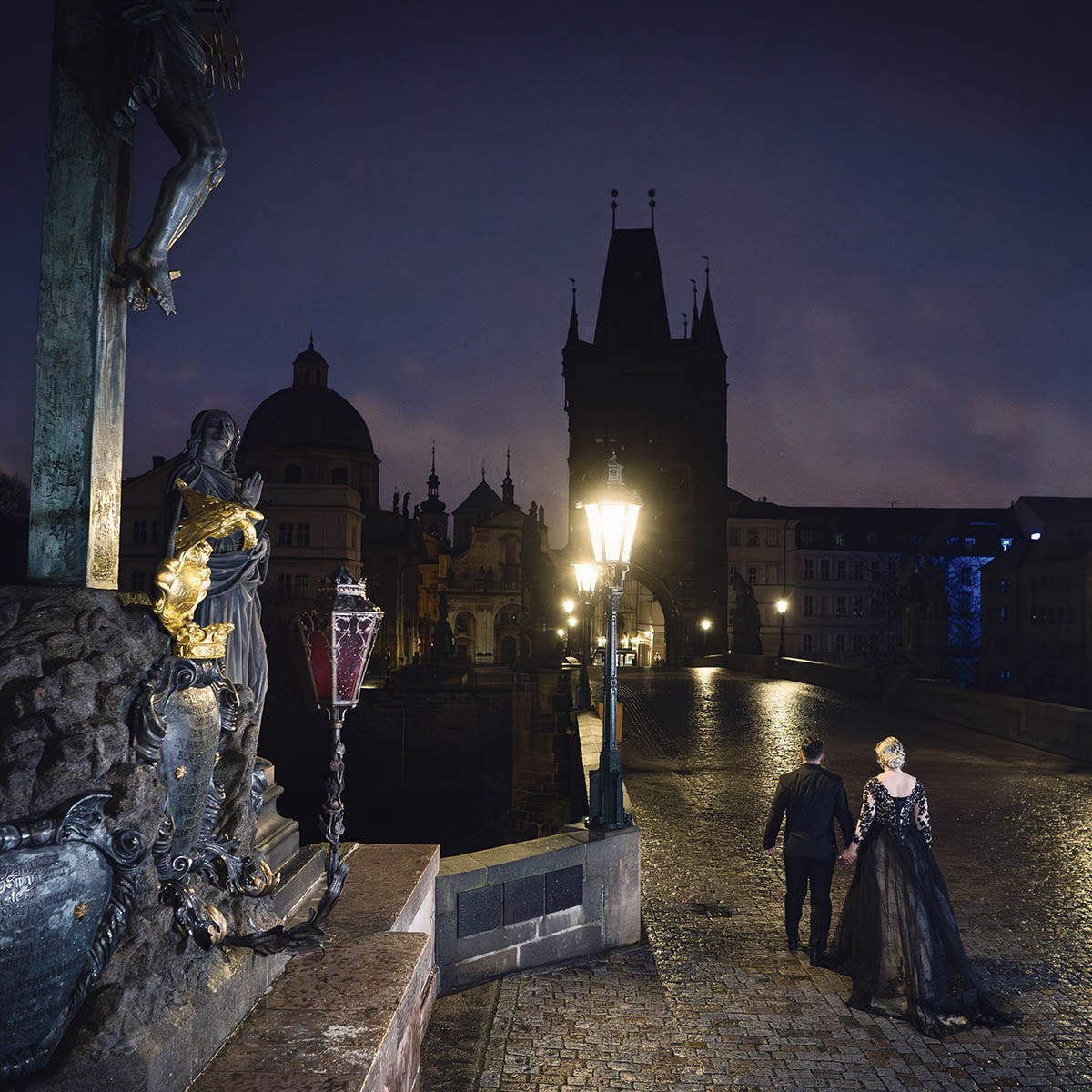 Couple in black walking alone during their gothic-inspired nighttime portrait session atop the Charles Bridge