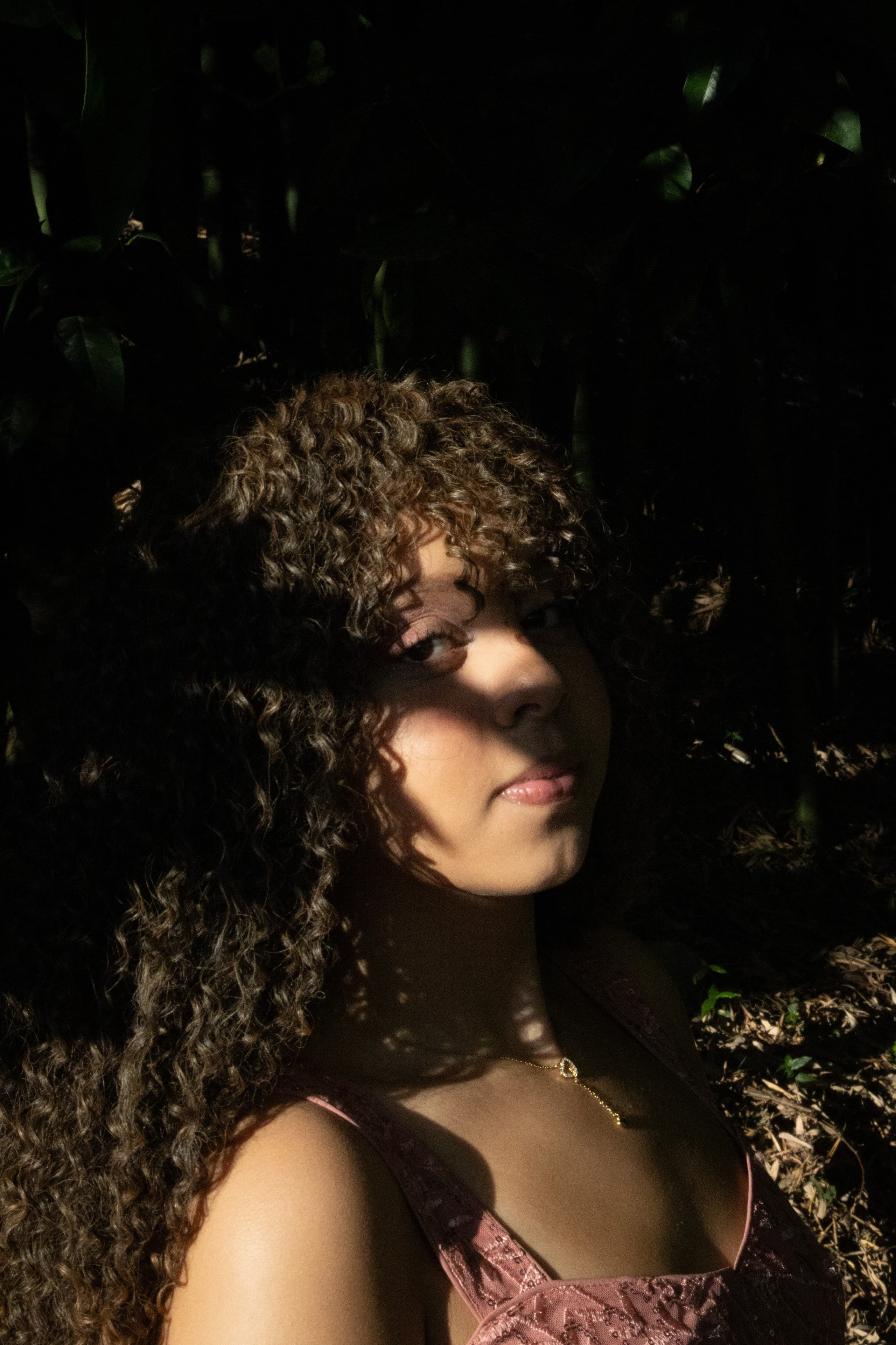Retrato conceitual de jovem com cabelos cacheados olhando para a câmera com jogo de luz e sombra forte em seu rosto.