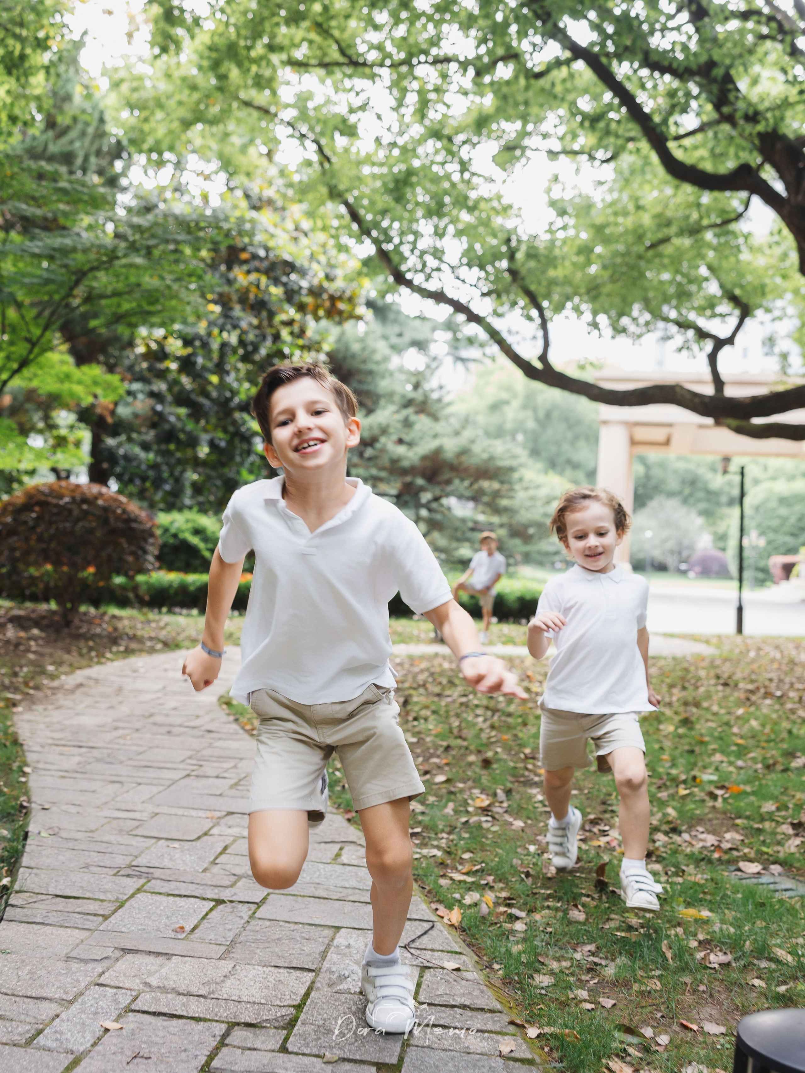 Two older kids running on a tree-lined path | Two children running freely along a sunlit path in the French Concession