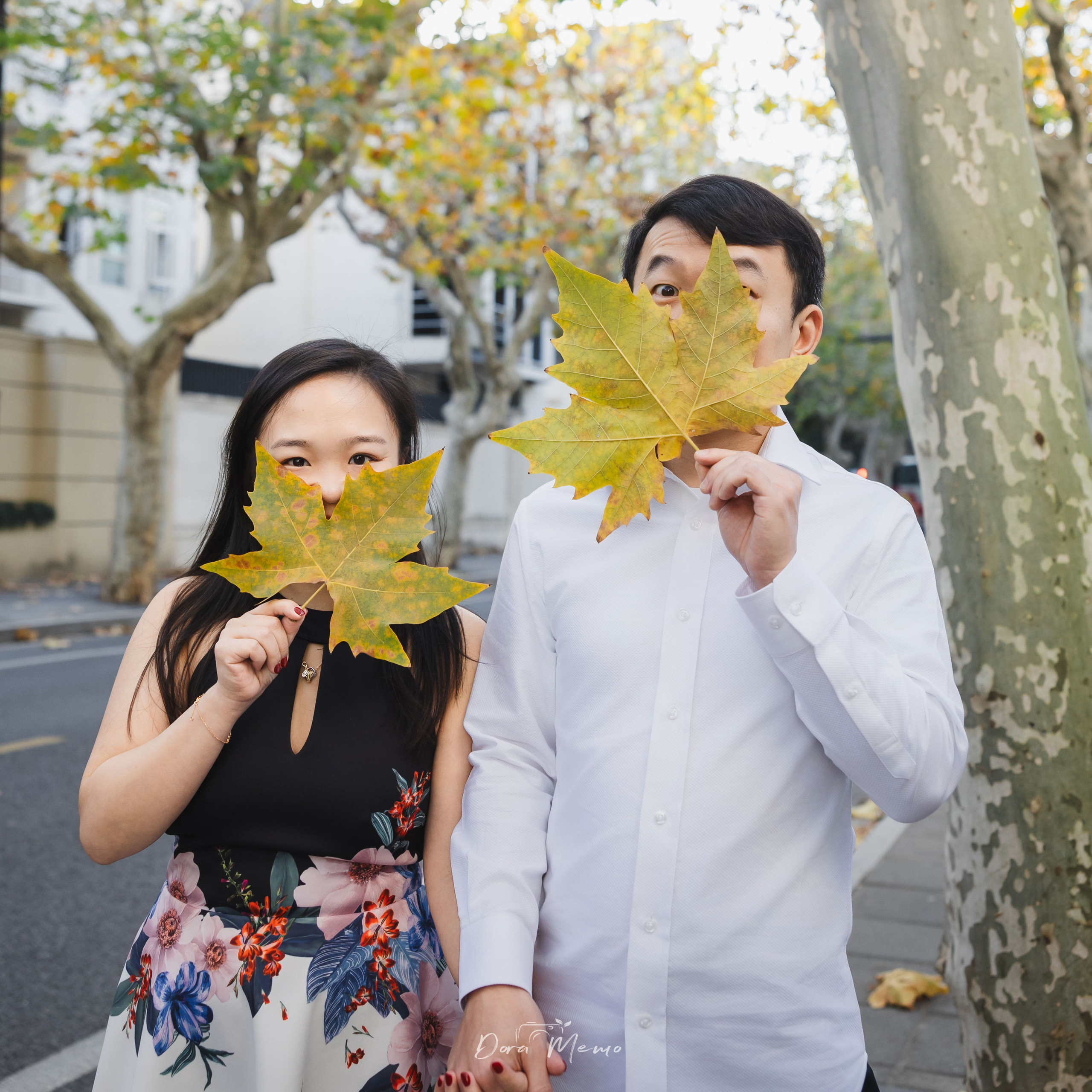  Couple playfully hiding behind autumn leaves during their engagement walk