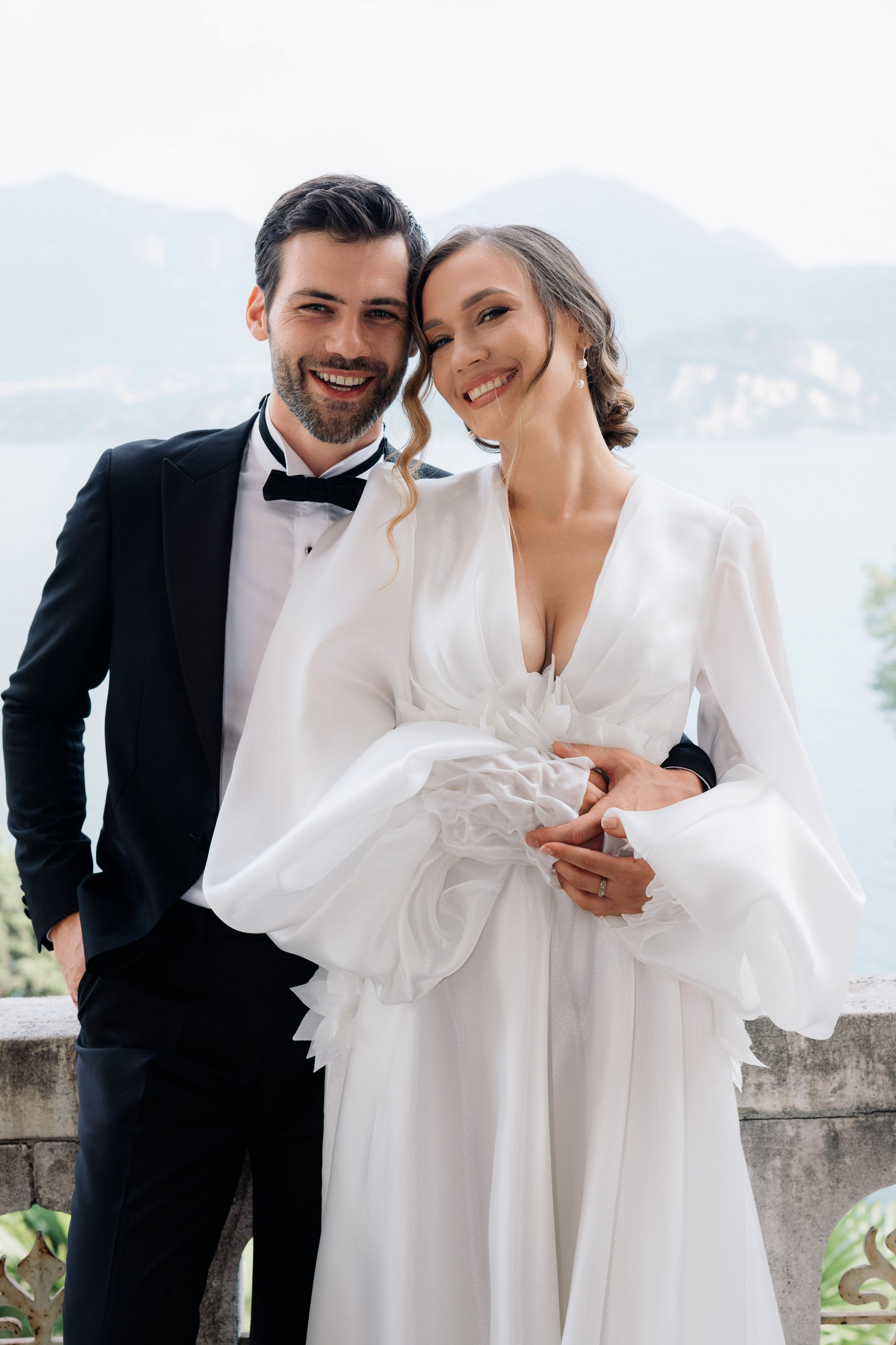 a bride and groom pose for a photo in front of the lake comoo