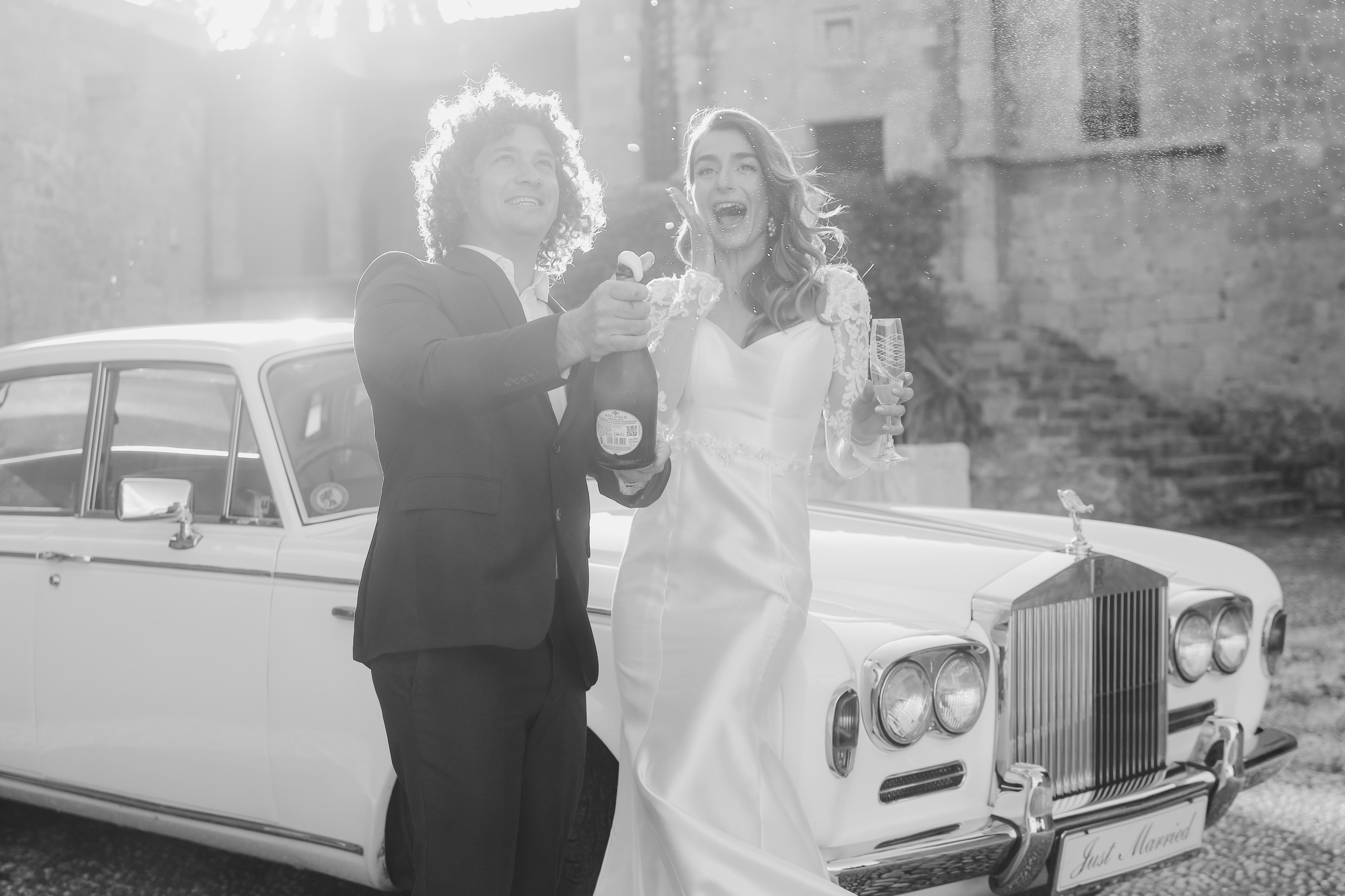 A bride and groom opening champaign next to Rolls Royce in old town of Rhodes island, Greece