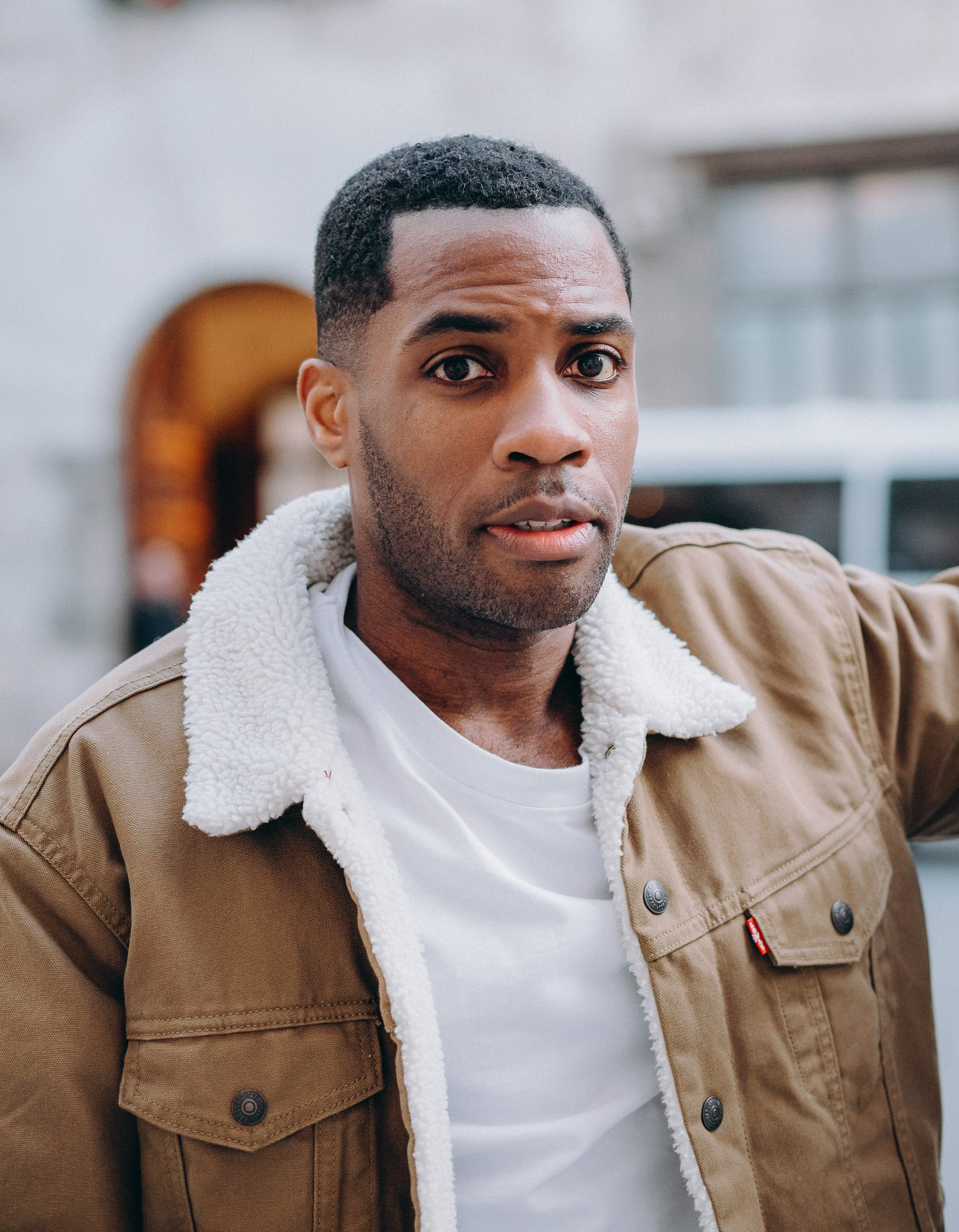 Мужская портретная фотосессия в Валенсии, Испания, с естественным крупным портретом мужчины с выразительным и уверенным взглядом, в повседневной куртке и белой футболке, снятым на открытом воздухе при мягком естественном свете с городским средиземноморским фоном — идеально для мужской портретной фотографии, lifestyle-фотосессий для мужчин, портретов при естественном освещении, персонального брендинга и профессиональных мужских фотосессий в Валенсии и по всей Испании.