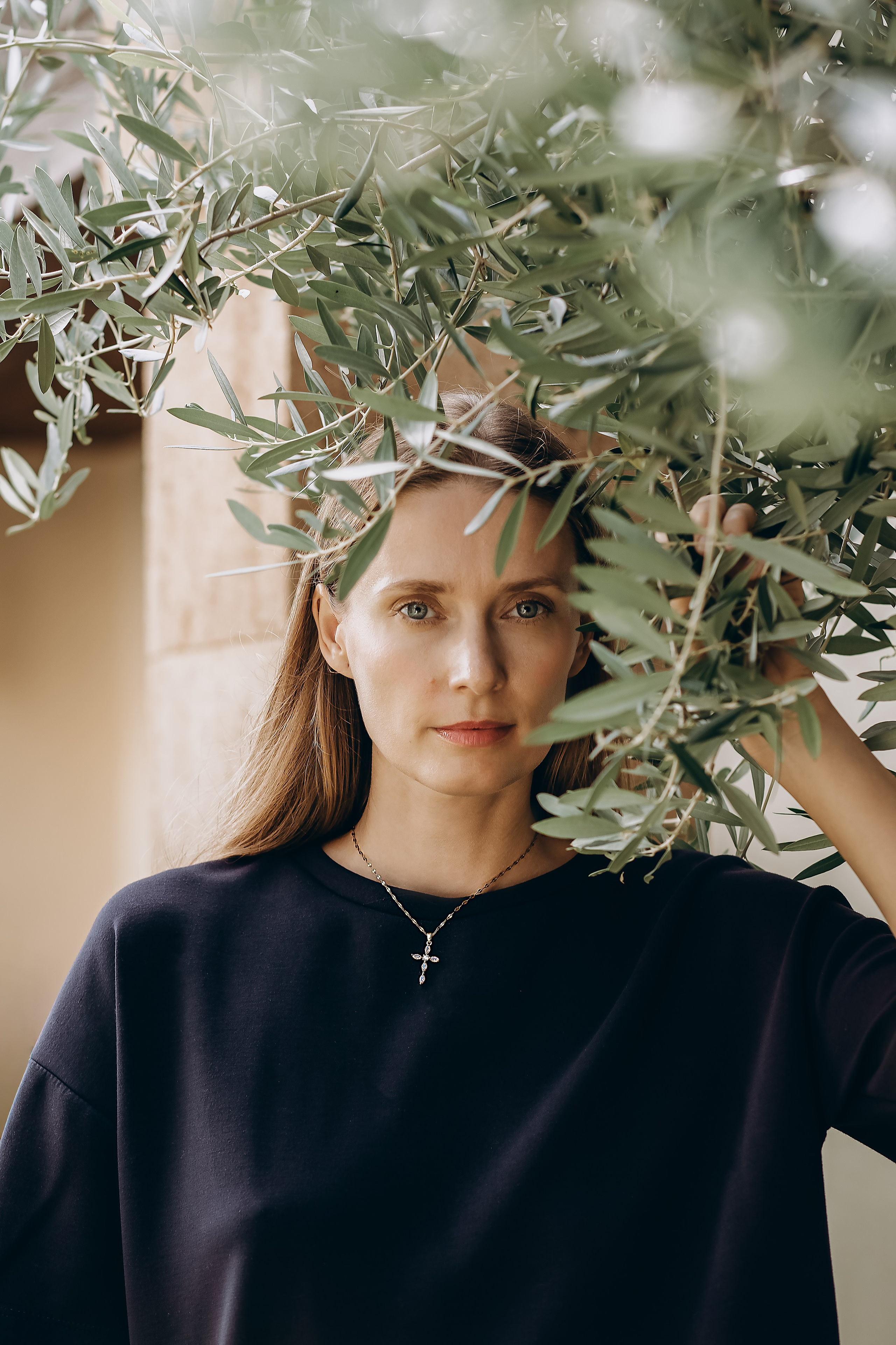 Natural brand portrait of a woman standing among olive branches, wearing a delicate cross necklace, captured during a content and product photoshoot in Valencia, Spain—ideal for showcasing ethical jewelry, nature-inspired branding, and lifestyle photography for brands in Spain.