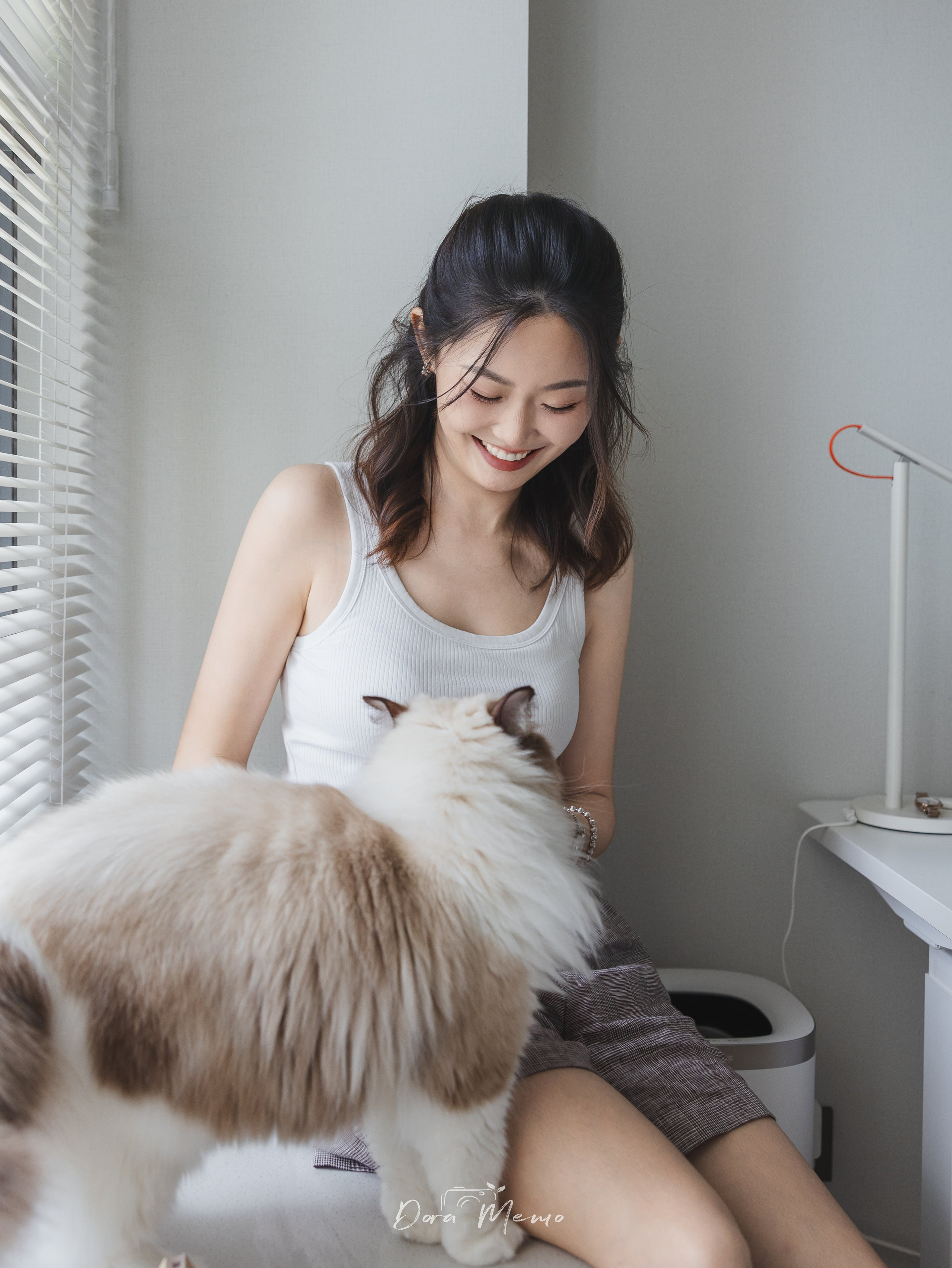 A smiling woman looks down at her ragdoll cat in soft window light — natural and candid portrait by a Shanghai lifestyle and family photographer.