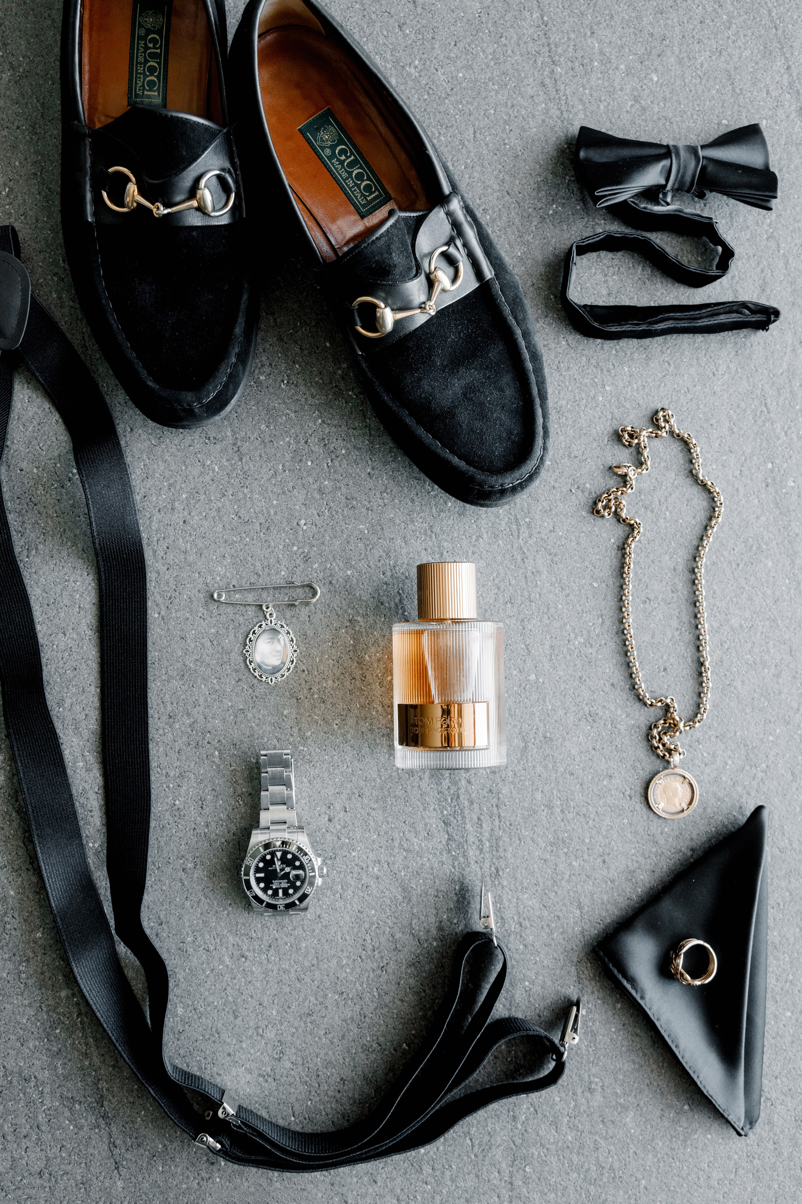 Groom’s black leather moccasins beside a satin black bow tie, and a geometric-patterned pocket square, styled for a modern sharp look.