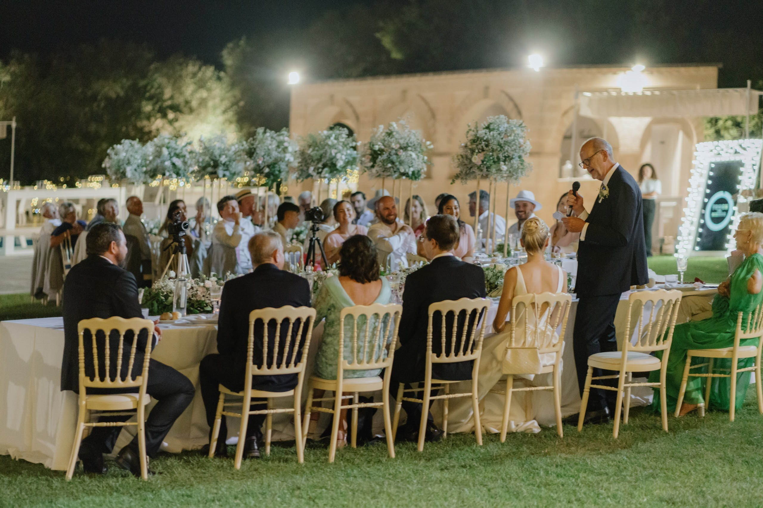 Guests seated at dinner under warm lights in Italian courtyard, atmospheric destination wedding photography in Ostuni Italy