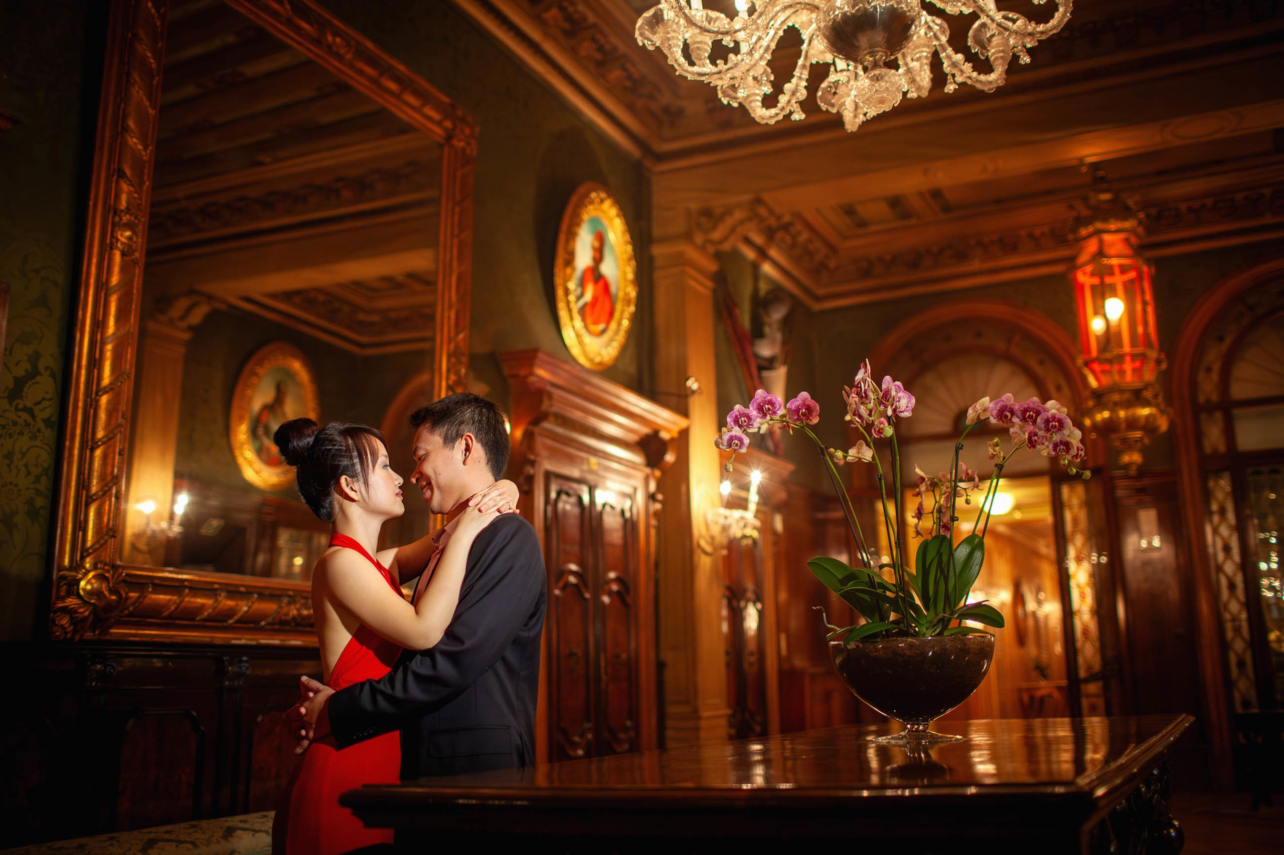 Thai woman in red evening dress with partner amid opulent architecture of Hotel Danieli Venice.