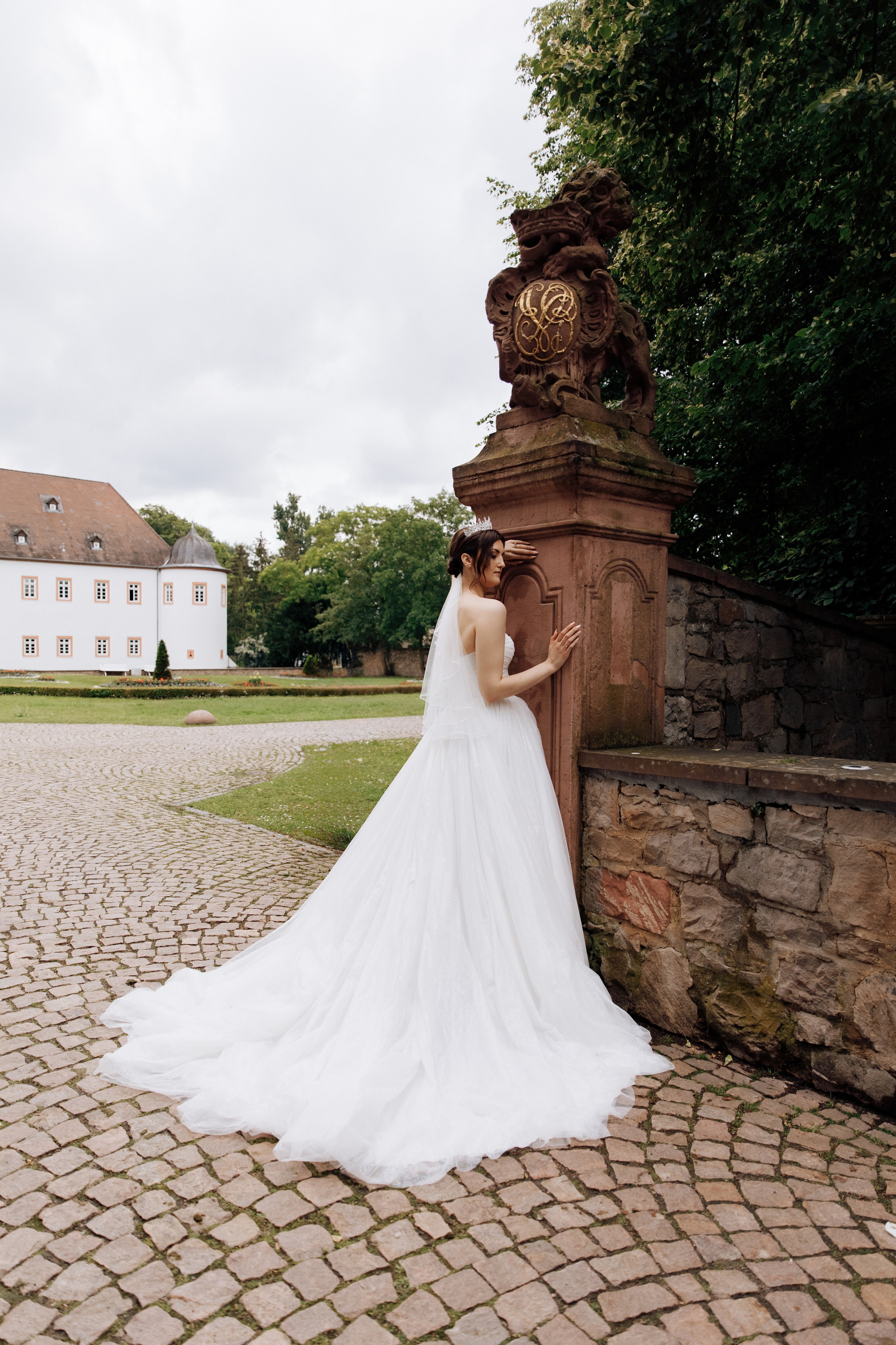 Die Braut steht neben einer antiken Säule, wobei ihr prachtvoller Schleppe des Hochzeitskleides sichtbar ist. 