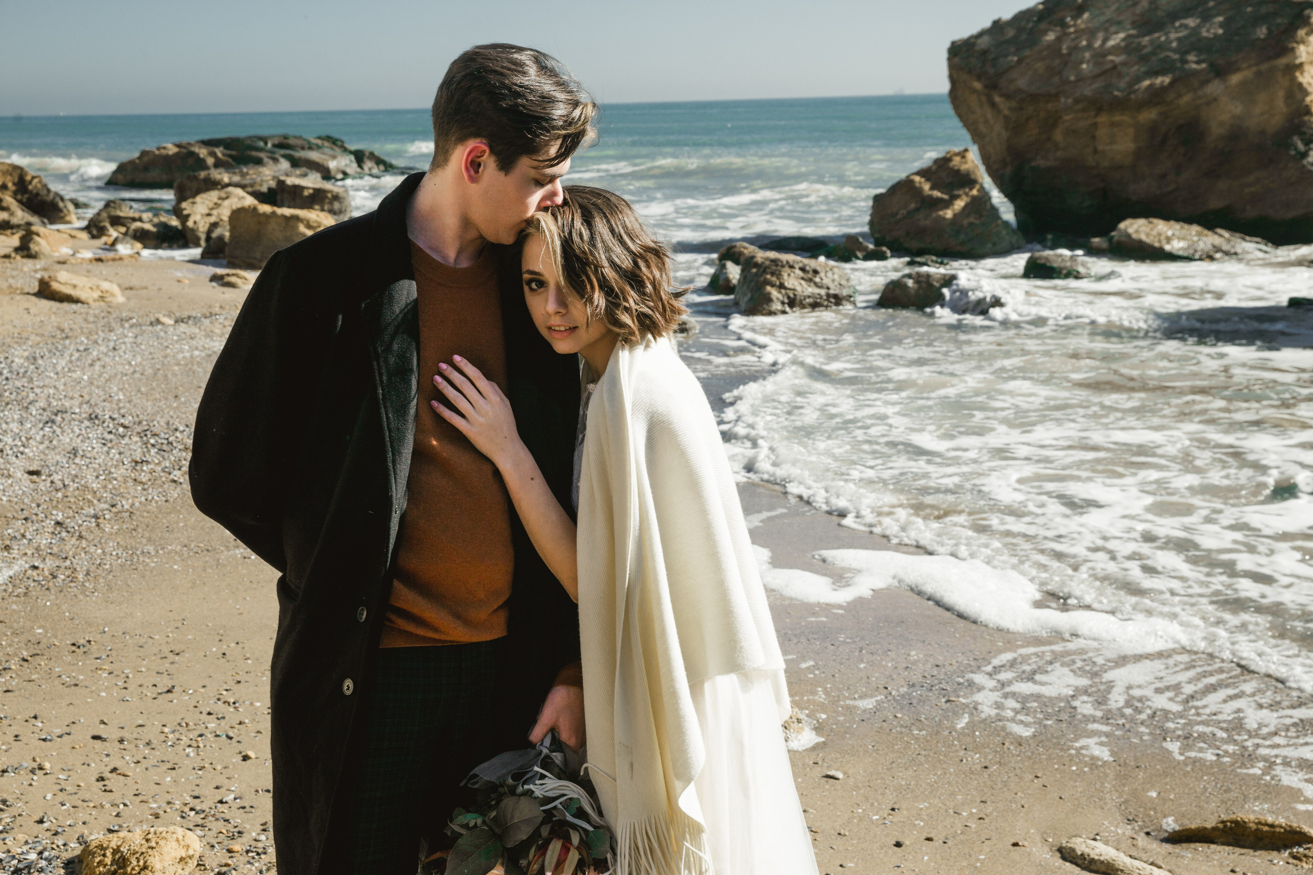 Bride with bouquet walking along sandy beach, destination wedding Spain