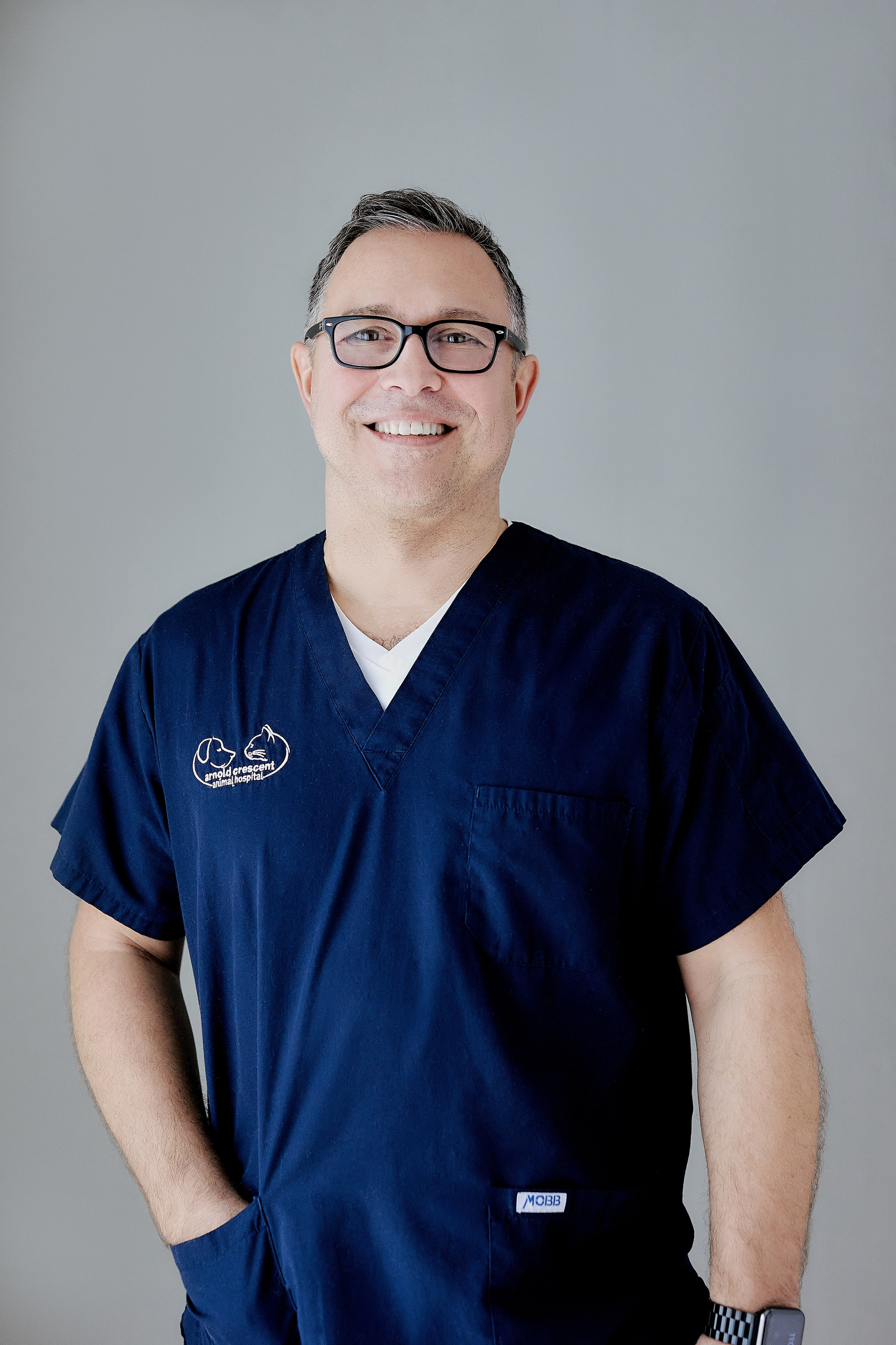 headshot of vet wearing blue scrubs, glasses and hand in pocket of scrubs 