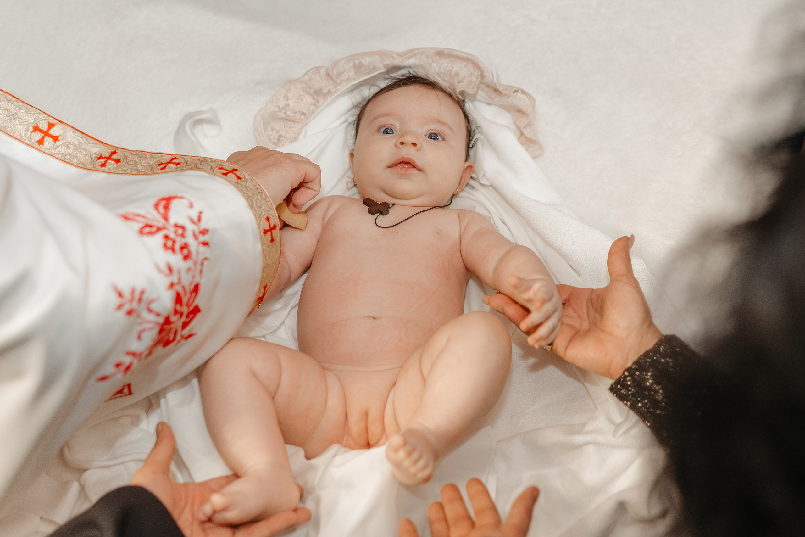 Nașa și moașa (nasa) îmbracă cu grijă pruncul Eveline Maria în hainele noi, după botez. Cadrul este intim, surprins din apropiere, concentrat pe momentul de îngrijire și tranziție de la ceremonie.