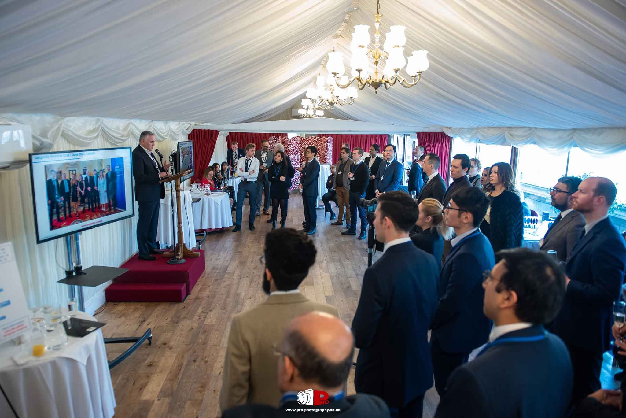 A businessman presenting at a corporate networking event with a screen displaying industry insights.