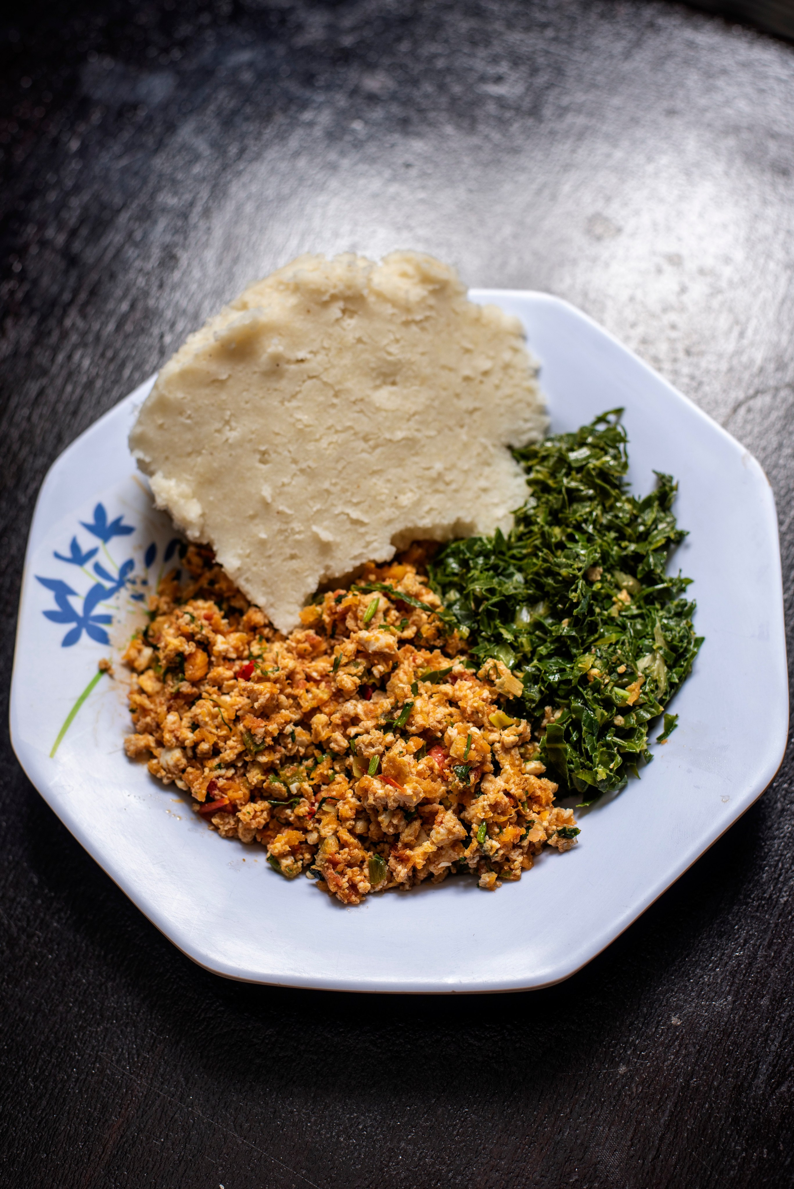 Traditional Kenyan dish: Ugali, eggs and sukuma wiki on white plate – local cuisine photography