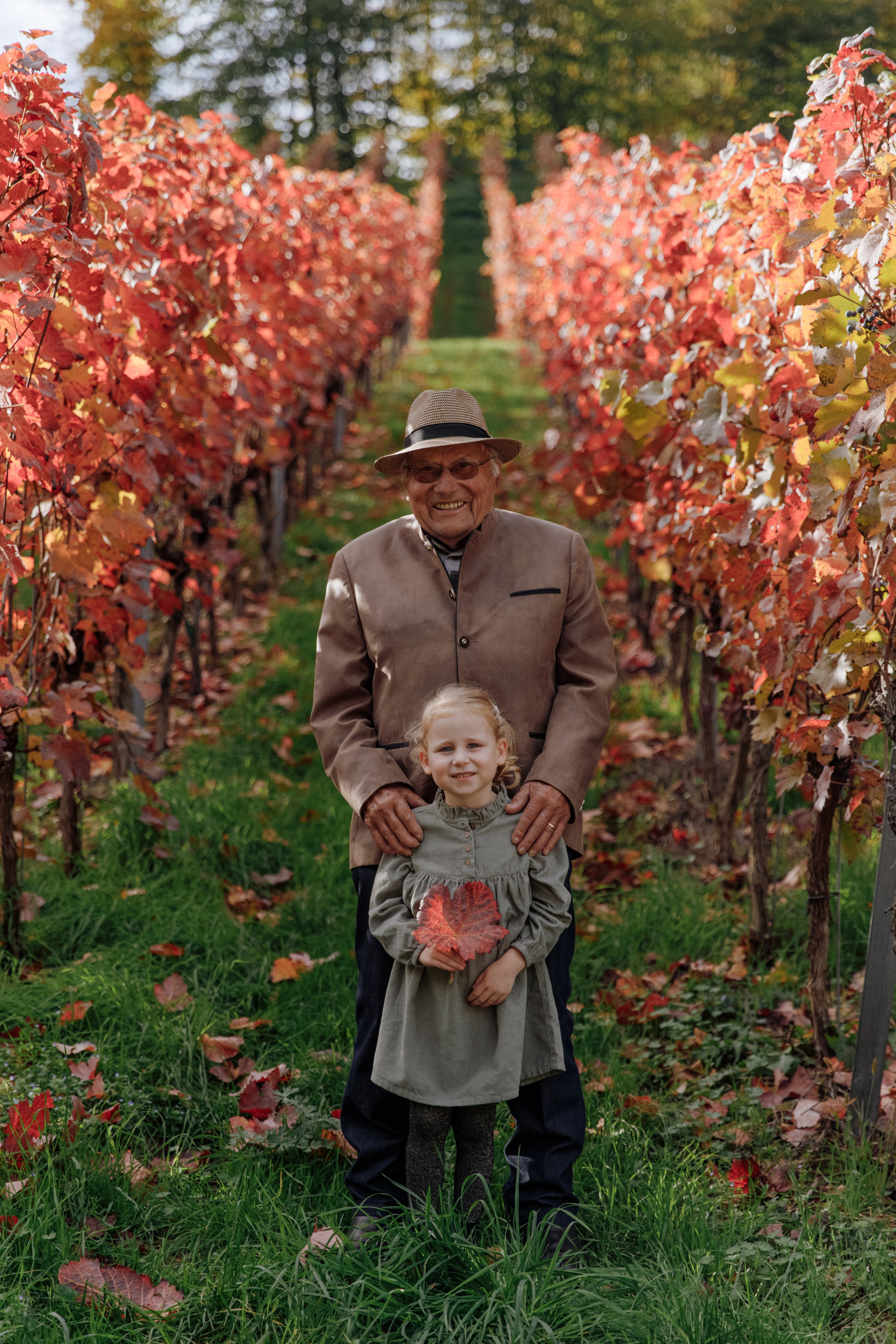 Ein Urgroßvater steht mit seiner Urenkelin im Weinberg und genießt einen gemeinsamen Moment.