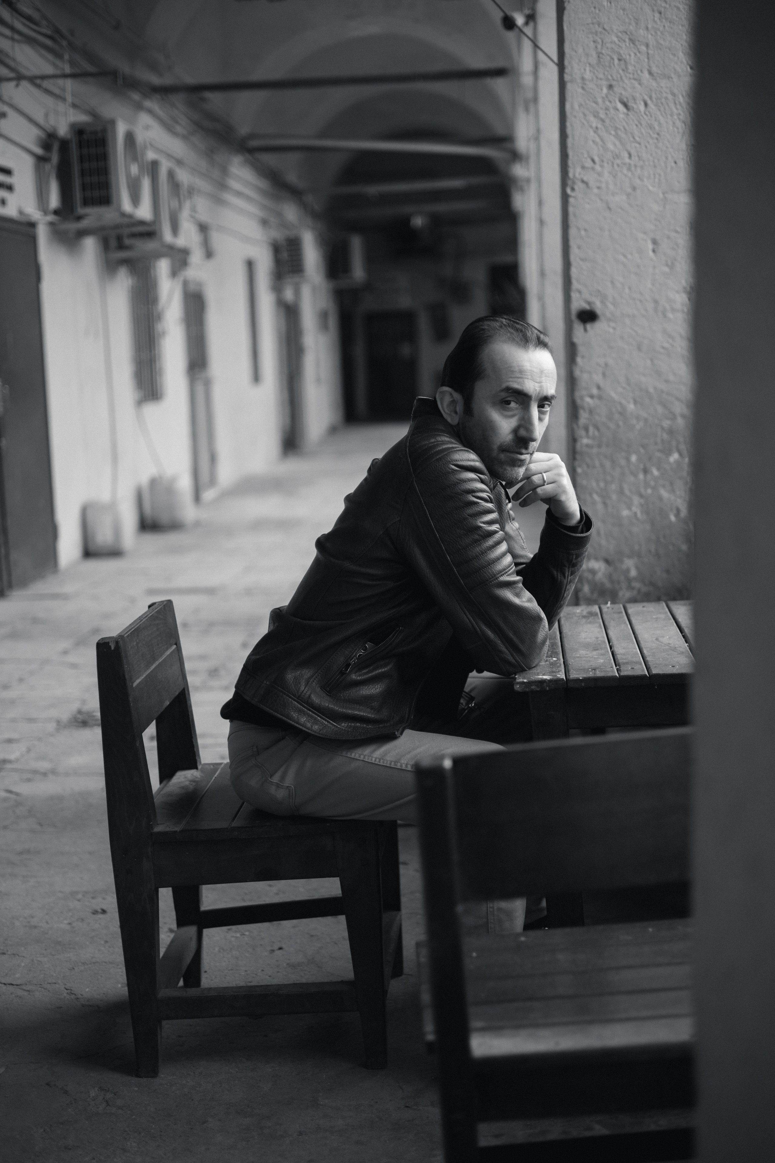 Мужской портрет в Стамбуле, мужчина сидит за деревянным столом в старинной аркаде, черно-белая фотография.