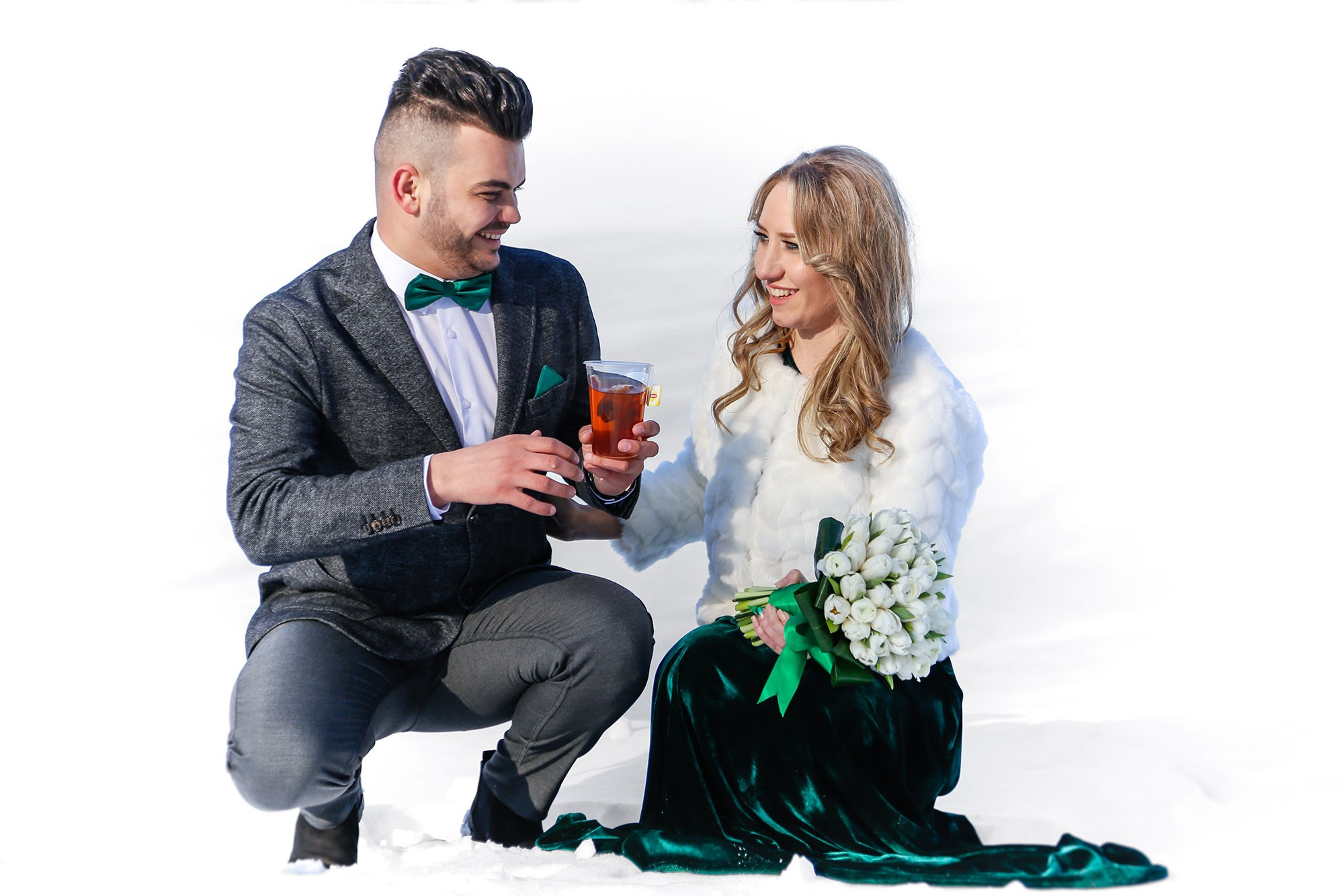 Smiling newlyweds holding mugs of hot tea to keep warm, a genuine and cozy moment captured in the white winter scenery.