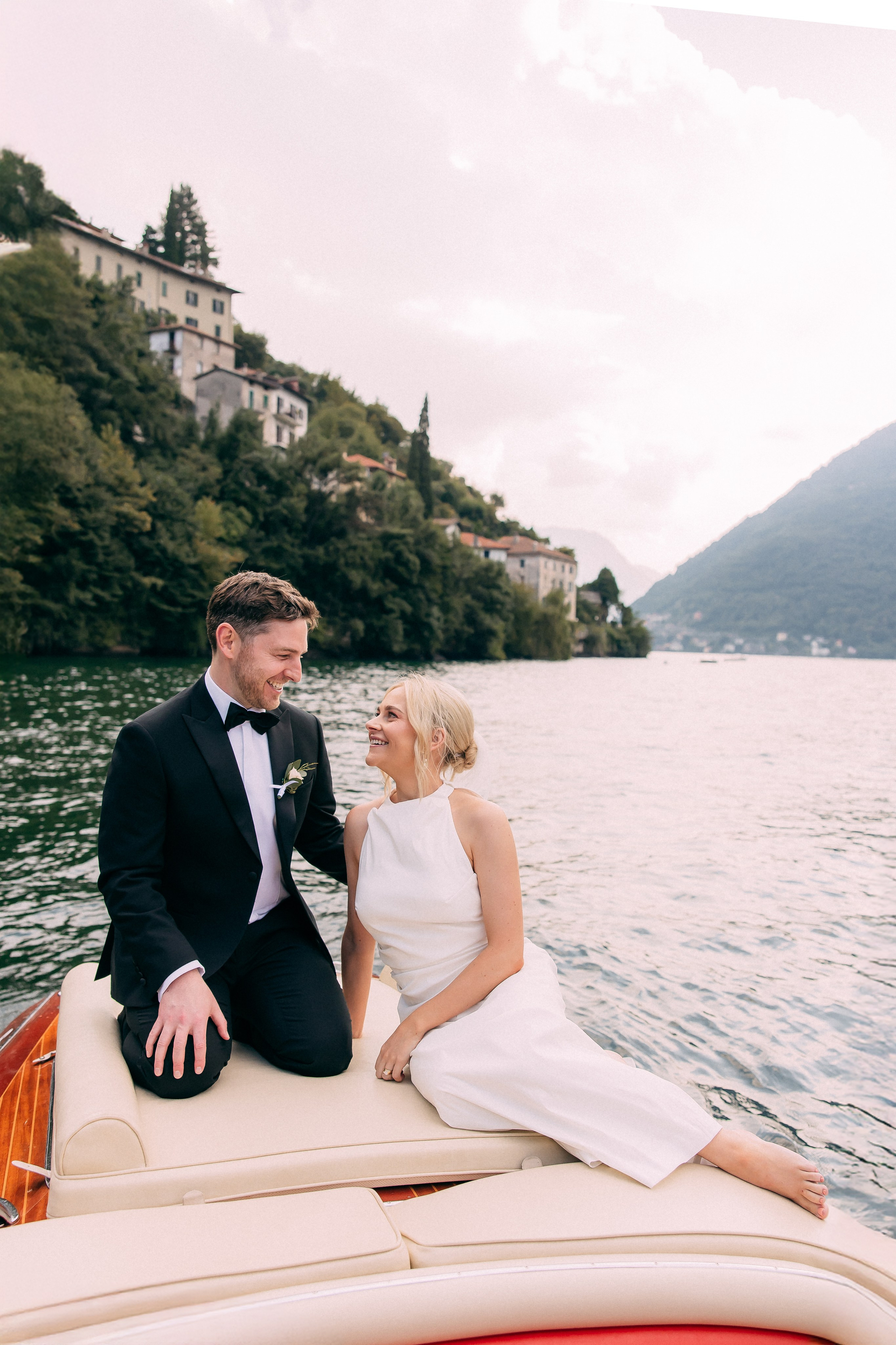 Bride and groom on a boat by the lakeside village at Villa Lario, Lake Como, Italy