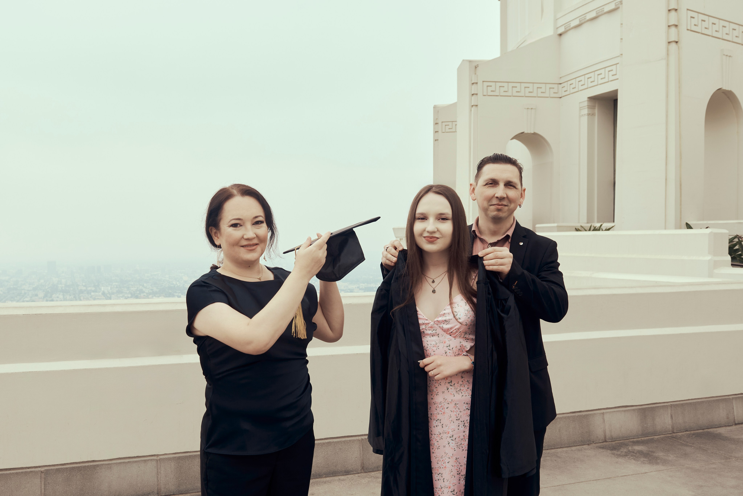 Graduate in cap and gown poses proudly with Los Angeles skyline in the background
