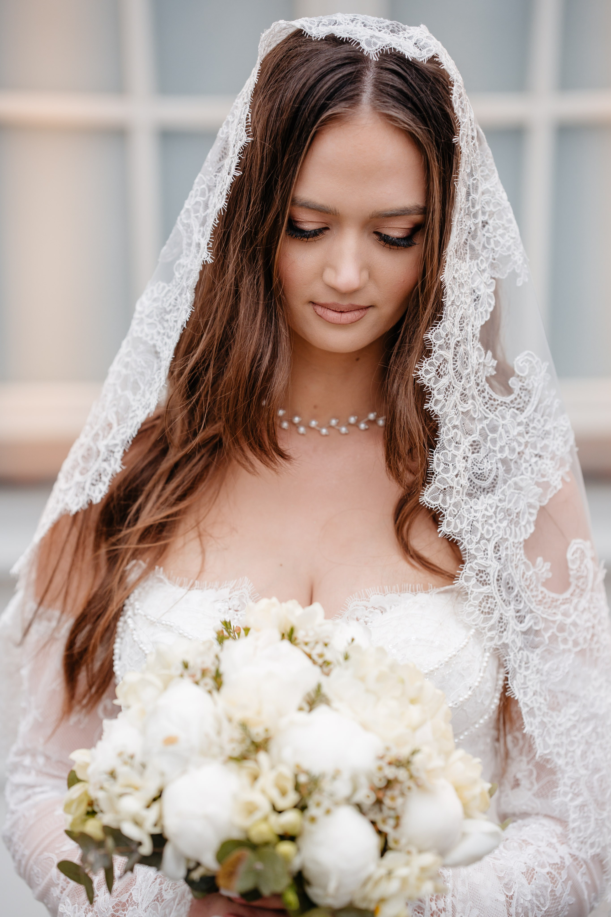Portret de mireasă cu voal din dantelă și buchet din bujori albi. Eleganță și rafinament în ziua nunții.