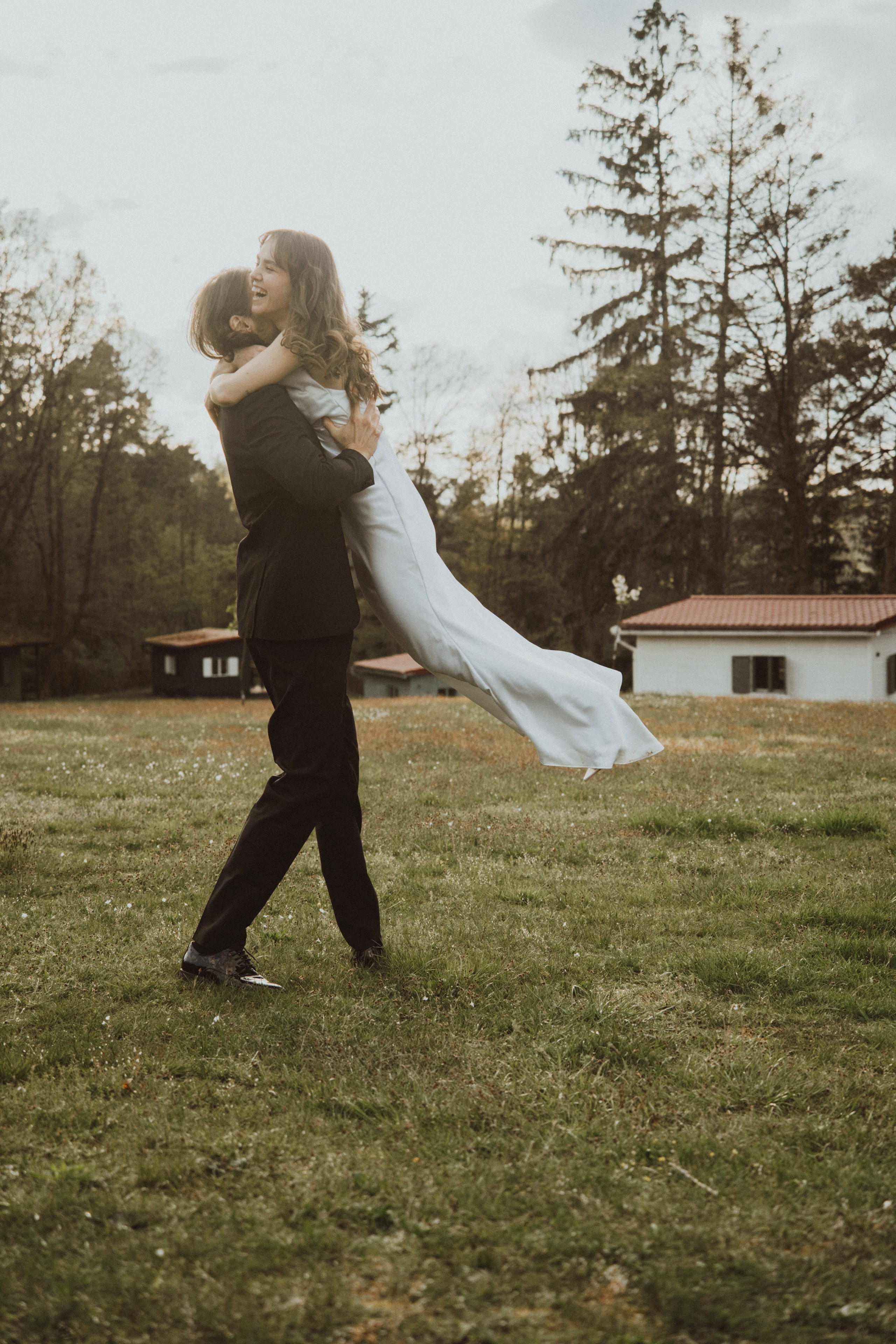 Romantická svatební fotografie nevěsty a ženicha v pohybu na zelení louce při západu slunce. Přirozené a emotivní zachycení lásky ve svatební den. 