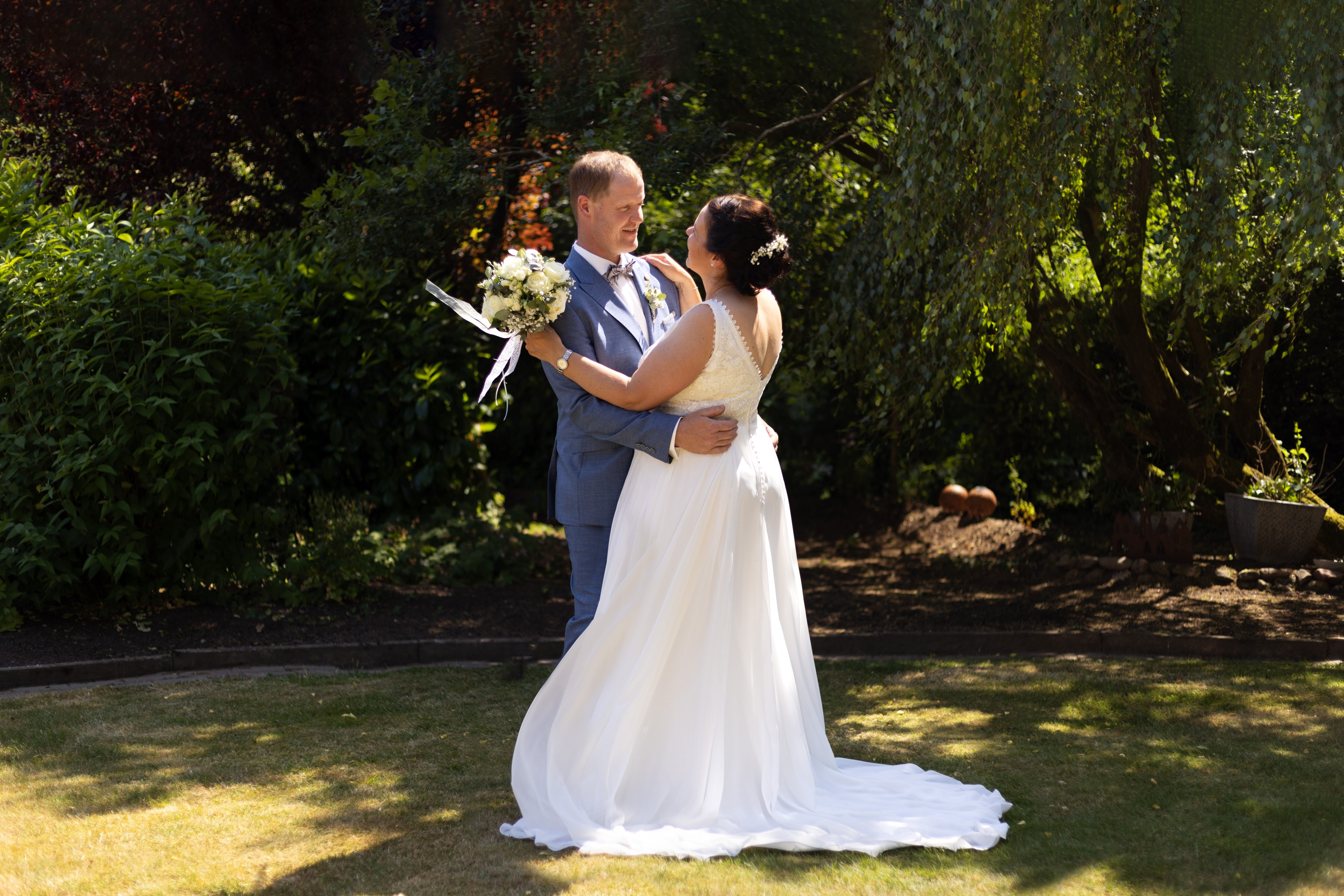Braut und Bräutigam bei einem liebevollen Moment im Garten ihres Hauses in Bippen.“