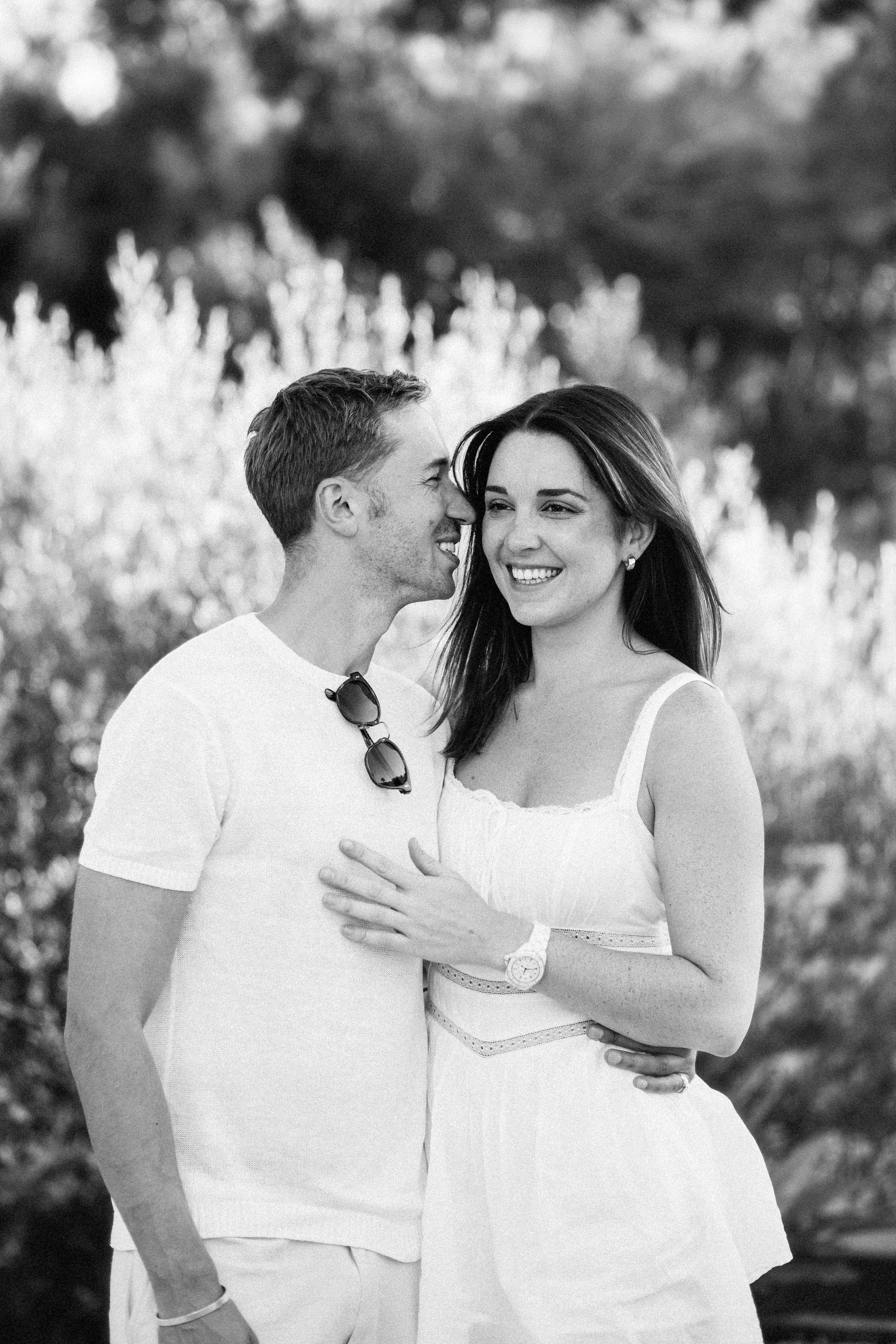 Joyful black and white portrait of a couple sharing a tender moment in a sunlit garden, captured during a romantic Love Story session in Valencia, Spain.