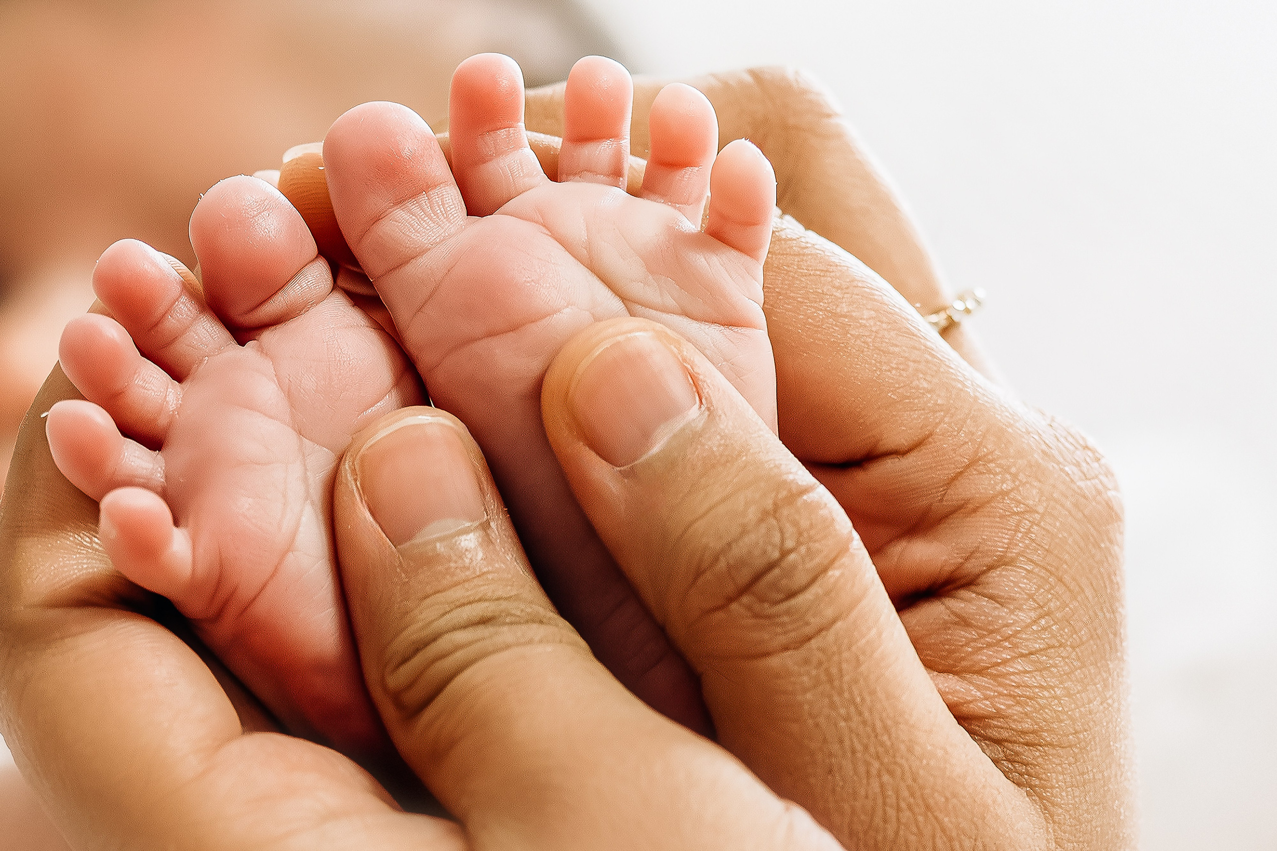 Семейная фотосессия в Валенсии, Испания, с крупным планом крошечных ножек новорождённого в руках родителей, снято в мягком тёплом свете для интимного, эмоционального и трогательного семейного момента — идеально для newborn и семейных фотосессий в Валенсии и по всей Испании.