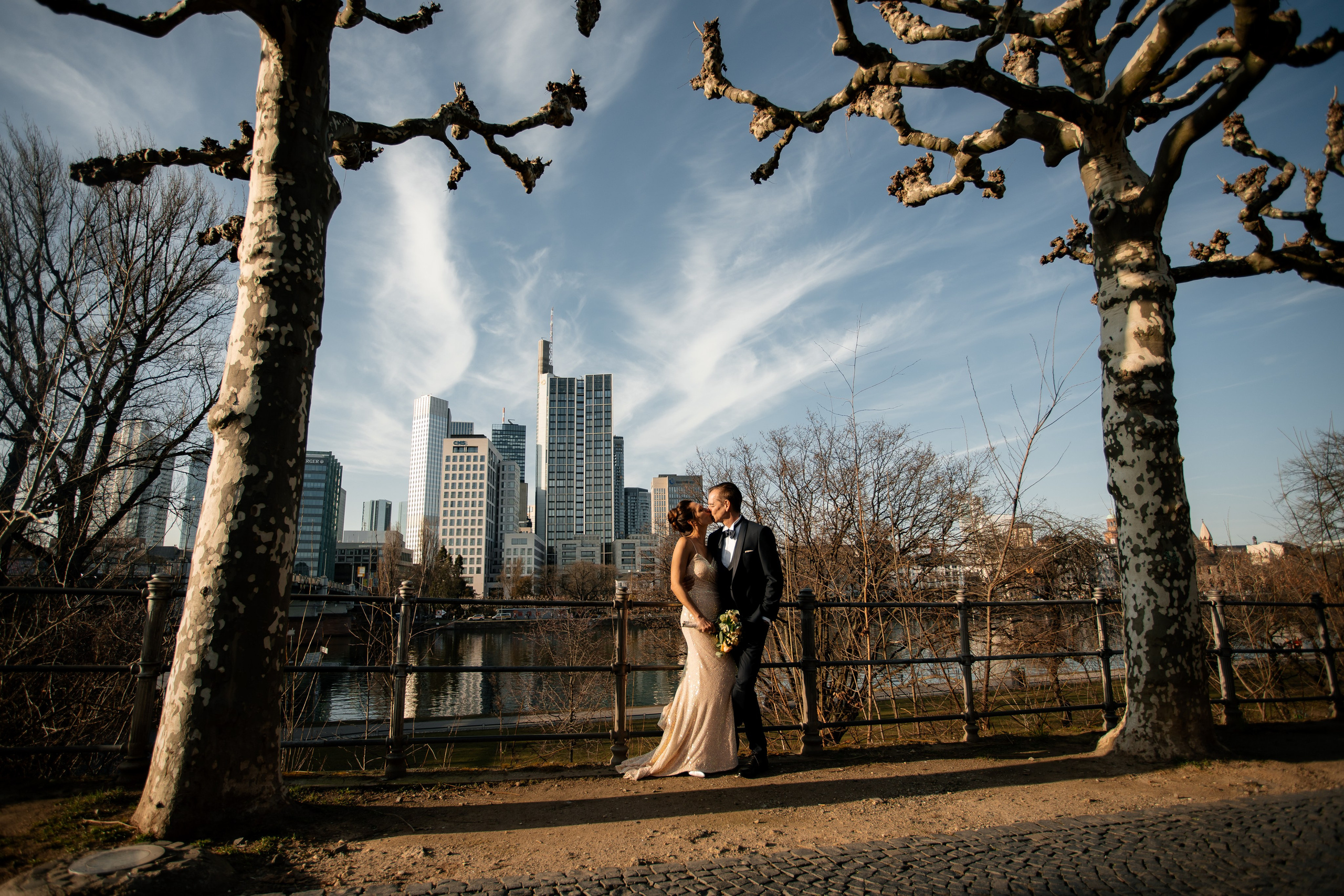 Brautpaar am Mainufer in Frankfurt zwischen alten Platanen mit Blick auf die Skyline und den Main Tower