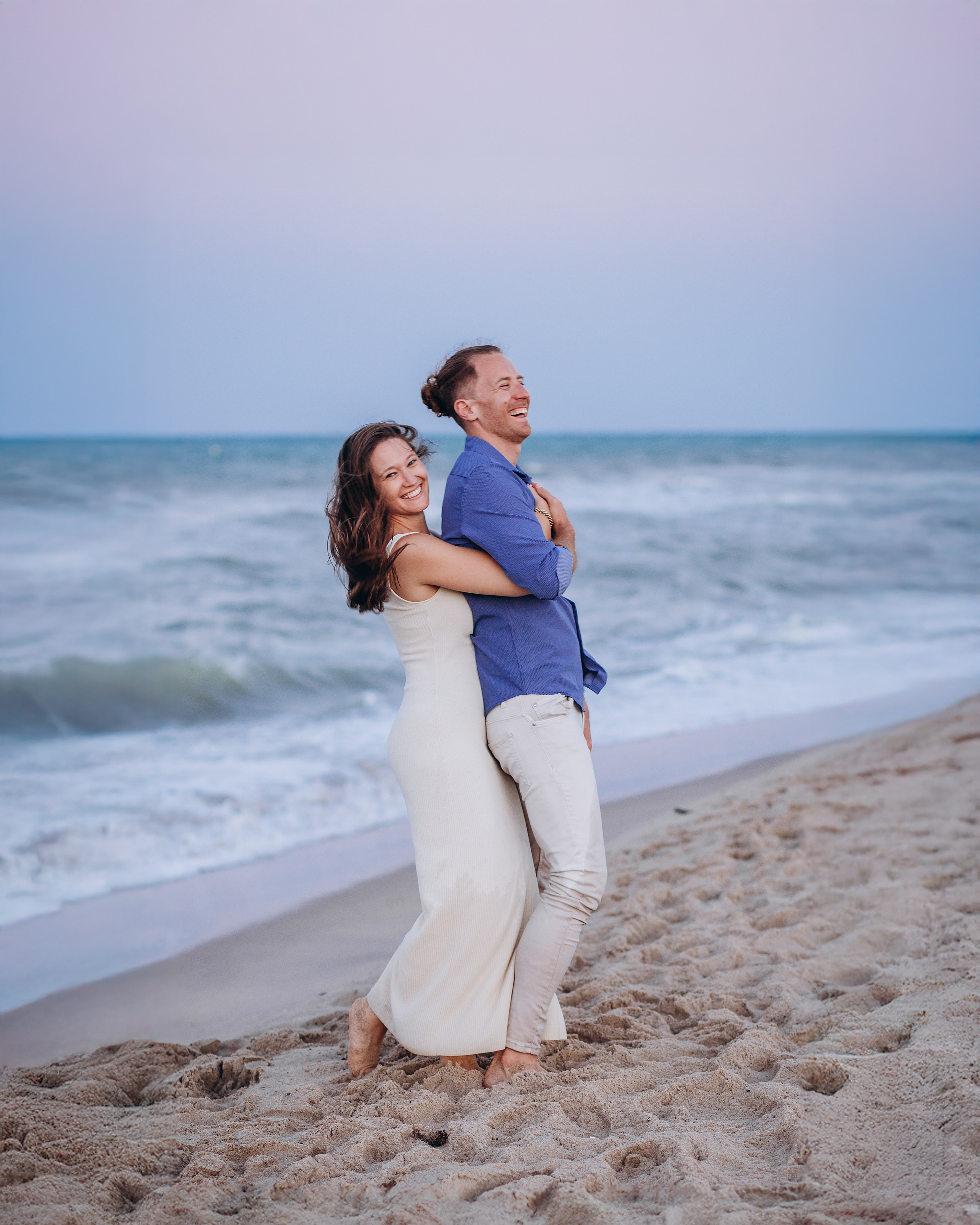 Pareja sonriendo y abrazándose en la playa al atardecer durante una sesión de fotos romántica en Valencia, España — inspiración perfecta para parejas que buscan sesiones fotográficas auténticas y alegres en la playa en Valencia y en toda España.