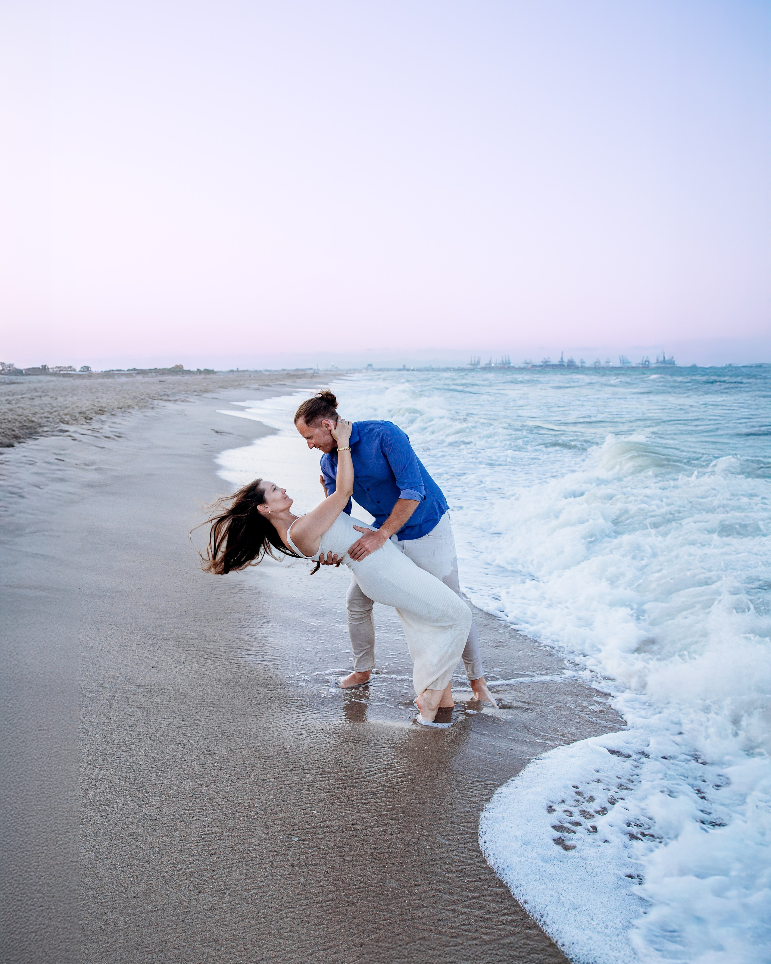 Sesión de fotos romántica en la playa de Valencia, España, con un hombre inclinando suavemente a su pareja junto a la orilla durante una sesión de love story al atardecer — inspiración perfecta para parejas que buscan sesiones fotográficas emocionales y elegantes en Valencia o en cualquier parte de España.