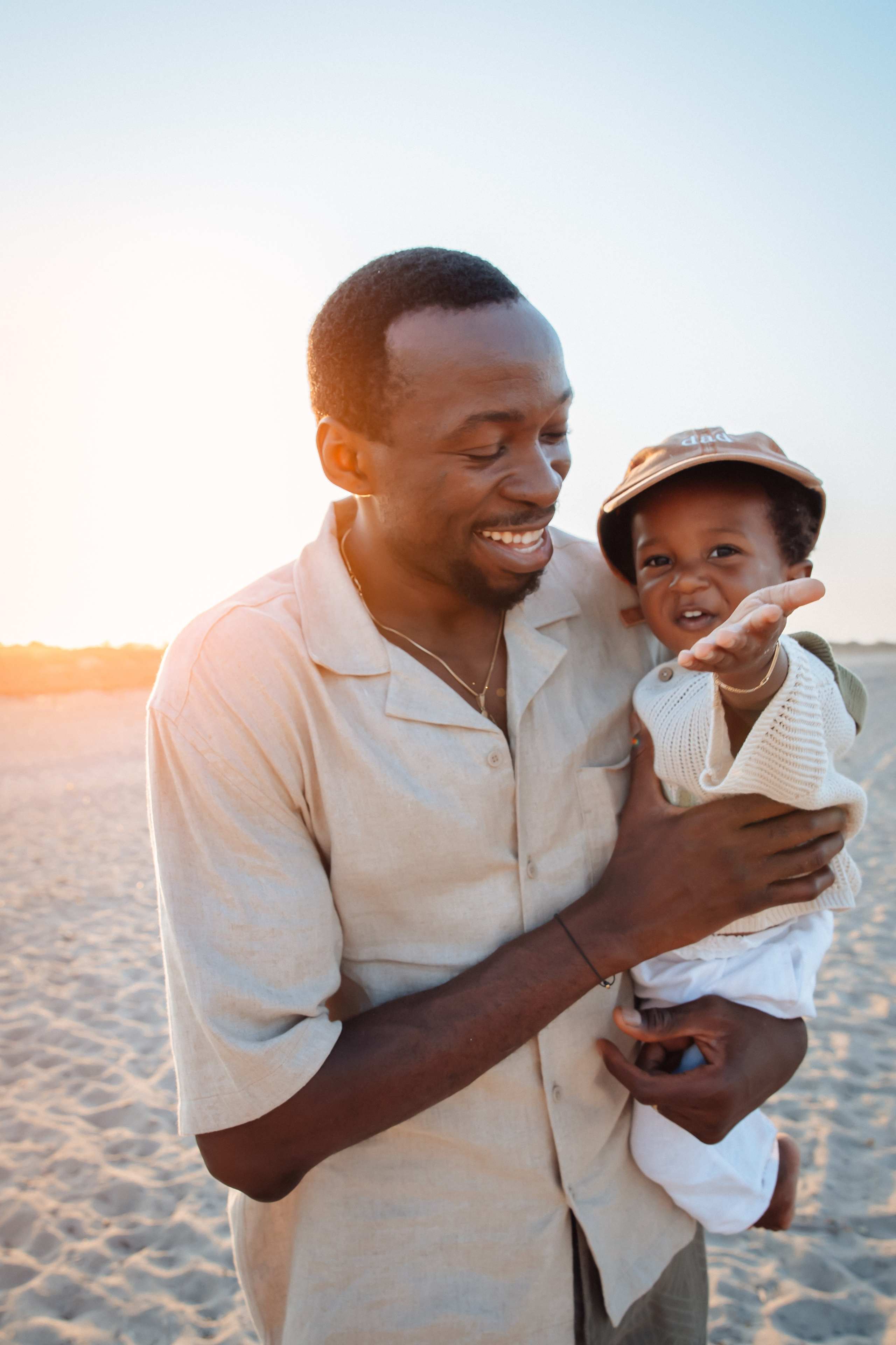 Momento alegre entre padre e hijo en la playa de Benidorm, España — retrato espontáneo de un padre sonriente sosteniendo a su hijo durante el atardecer, capturando amor, risas y conexión genuina.