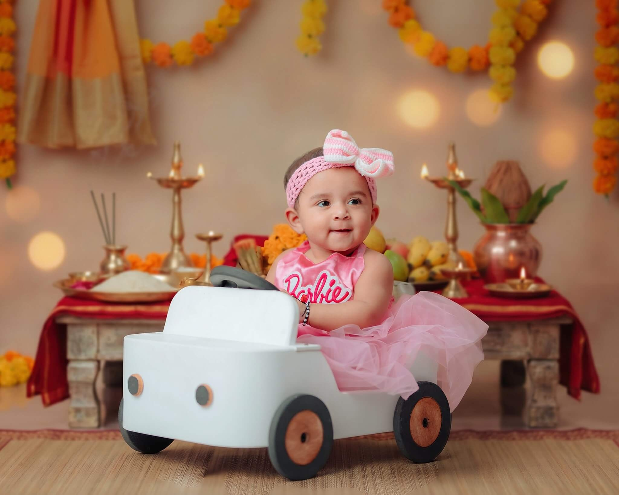 A sweet baby girl wearing a pink bow and sitting inside a white toy car for her birthday photography