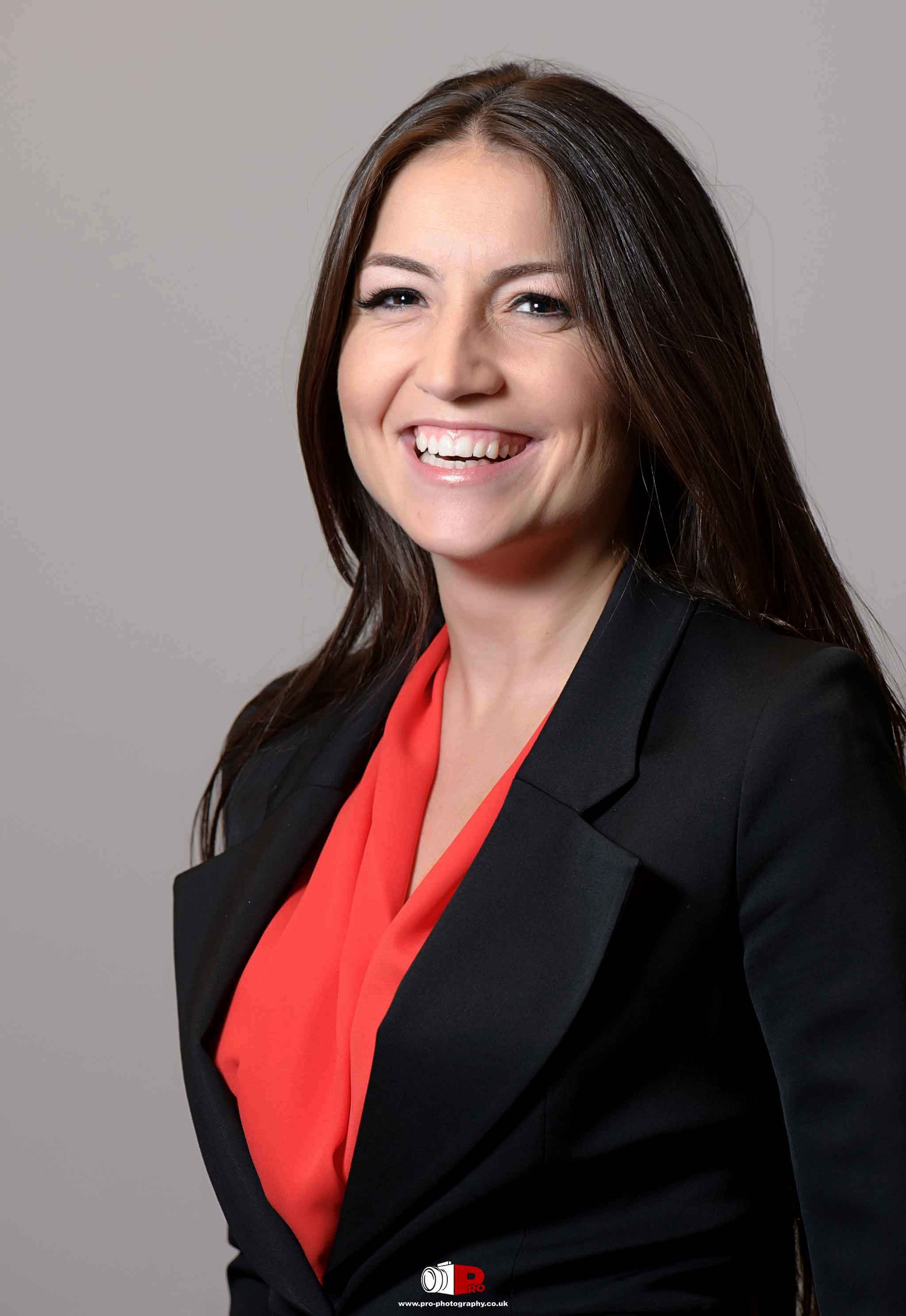 Businesswoman with long brown hair, smiling confidently while wearing a red blouse and black blazer.