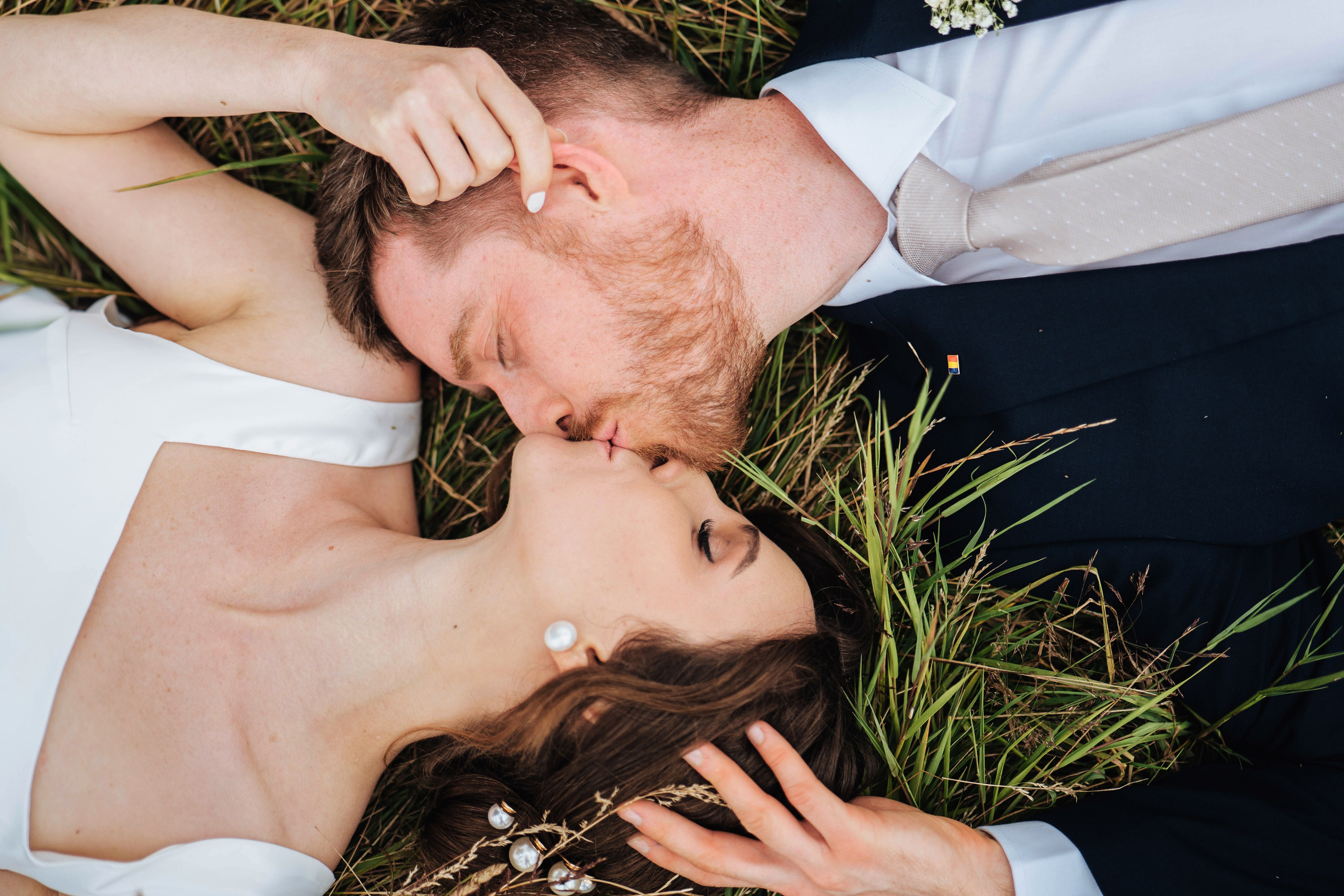 bride and groom kissing while laying on the grass