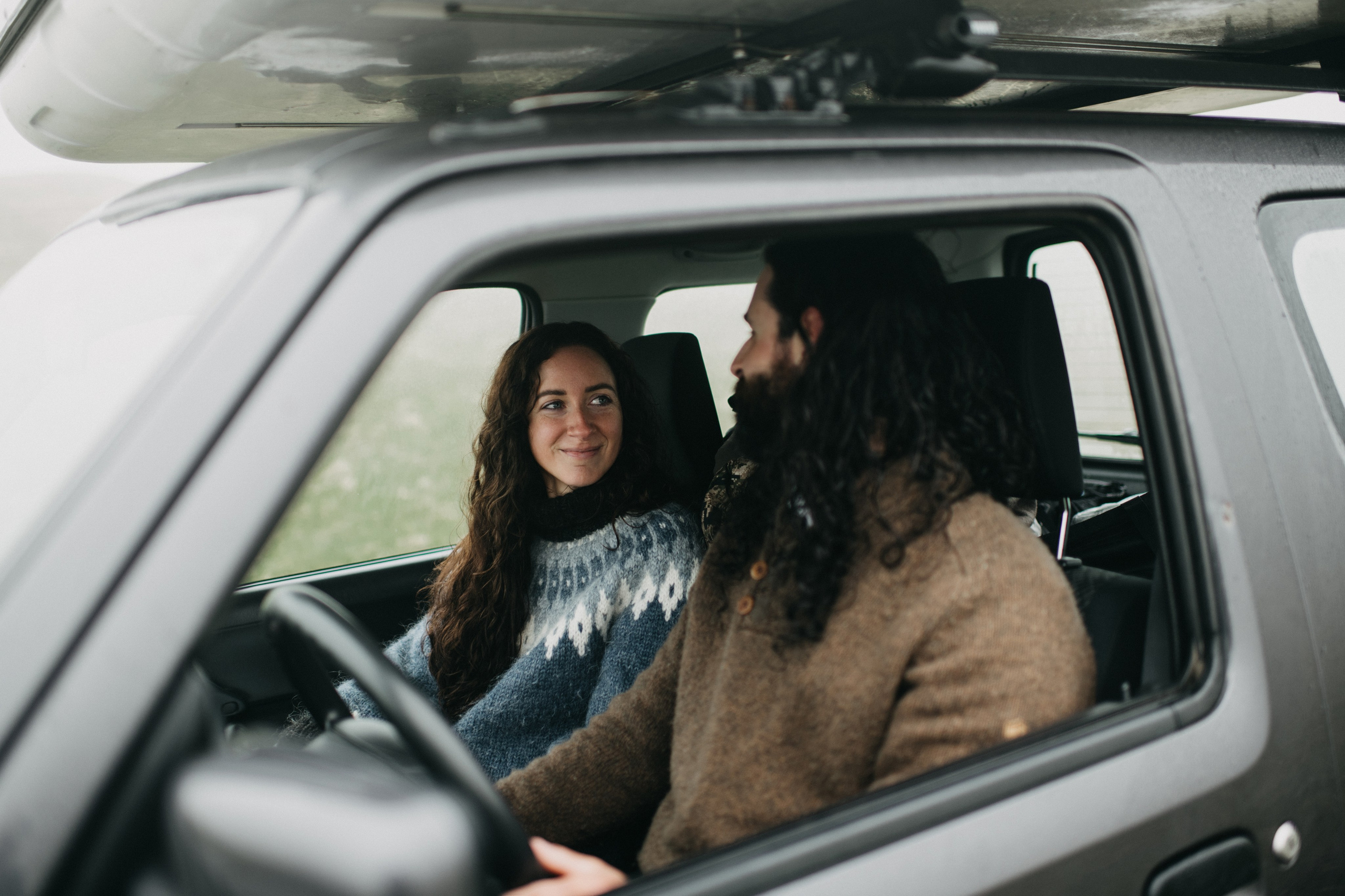 Bride and groom looking out over the vast, mysterious waters of Kleifarvatn, their wedding outfits contrasting against the dark landscape.