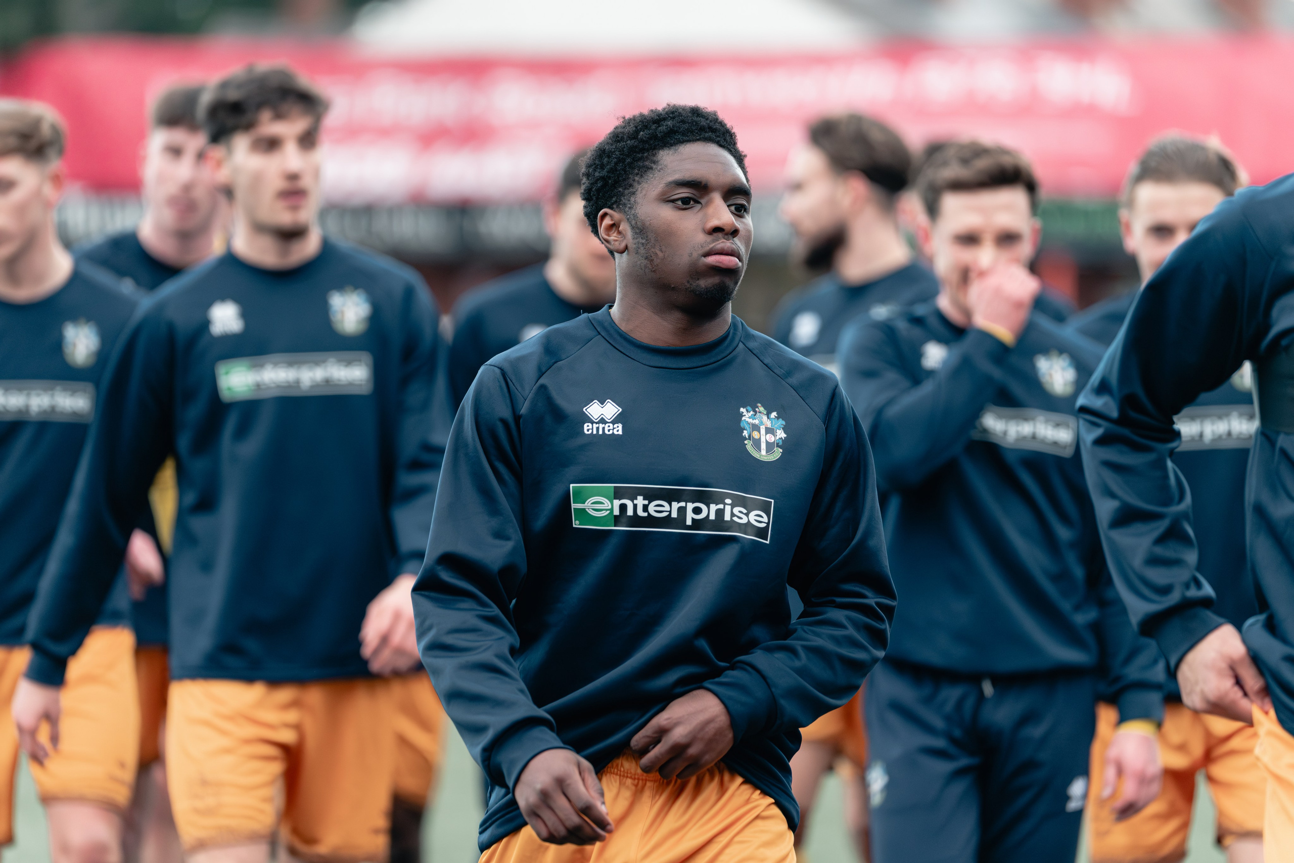 Sutton United player in training top and yellow shorts walks onto the pitch with teammates during pre-match warm-ups