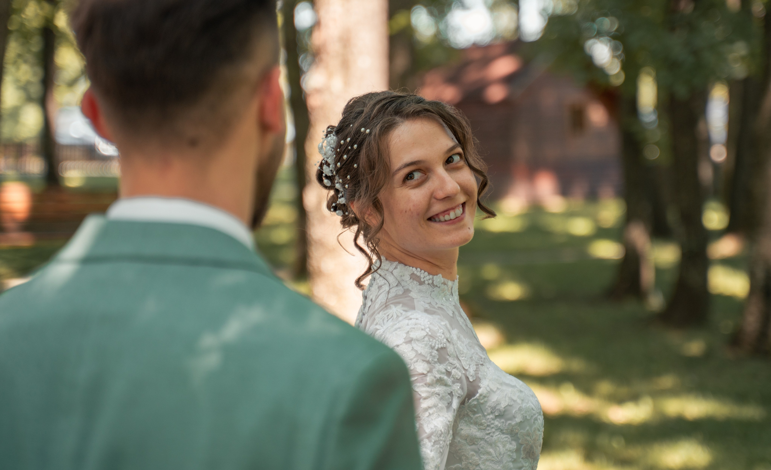 Mireasă zâmbind peste umăr către mire, portret de nuntă în aer liber, fotografii naturale de cuplu București, incadru.ro.