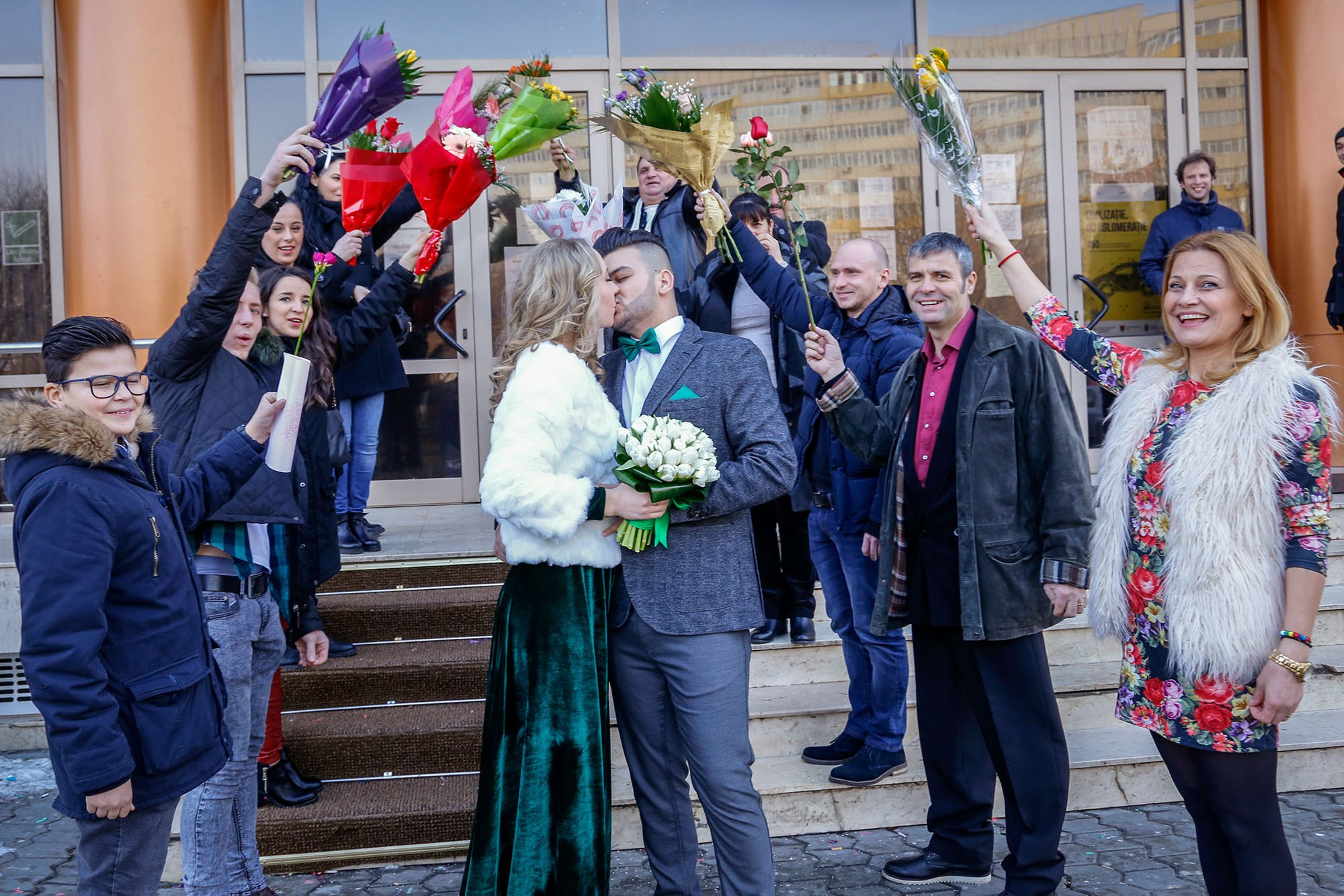 Newlyweds sharing a romantic kiss under the flower arch made by guests at the registry office exit.